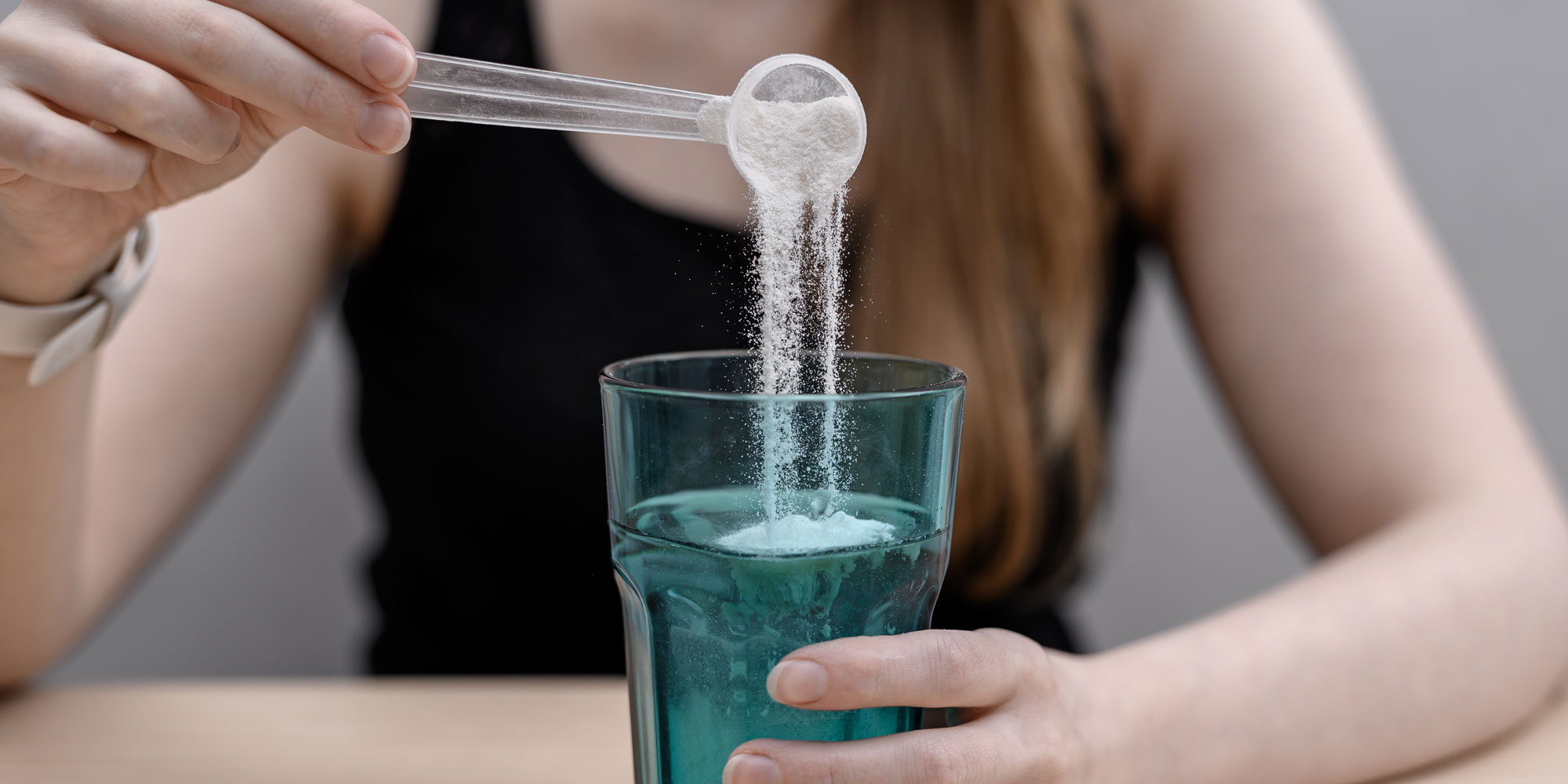 A person pouring collagen powder into a glass of water. 