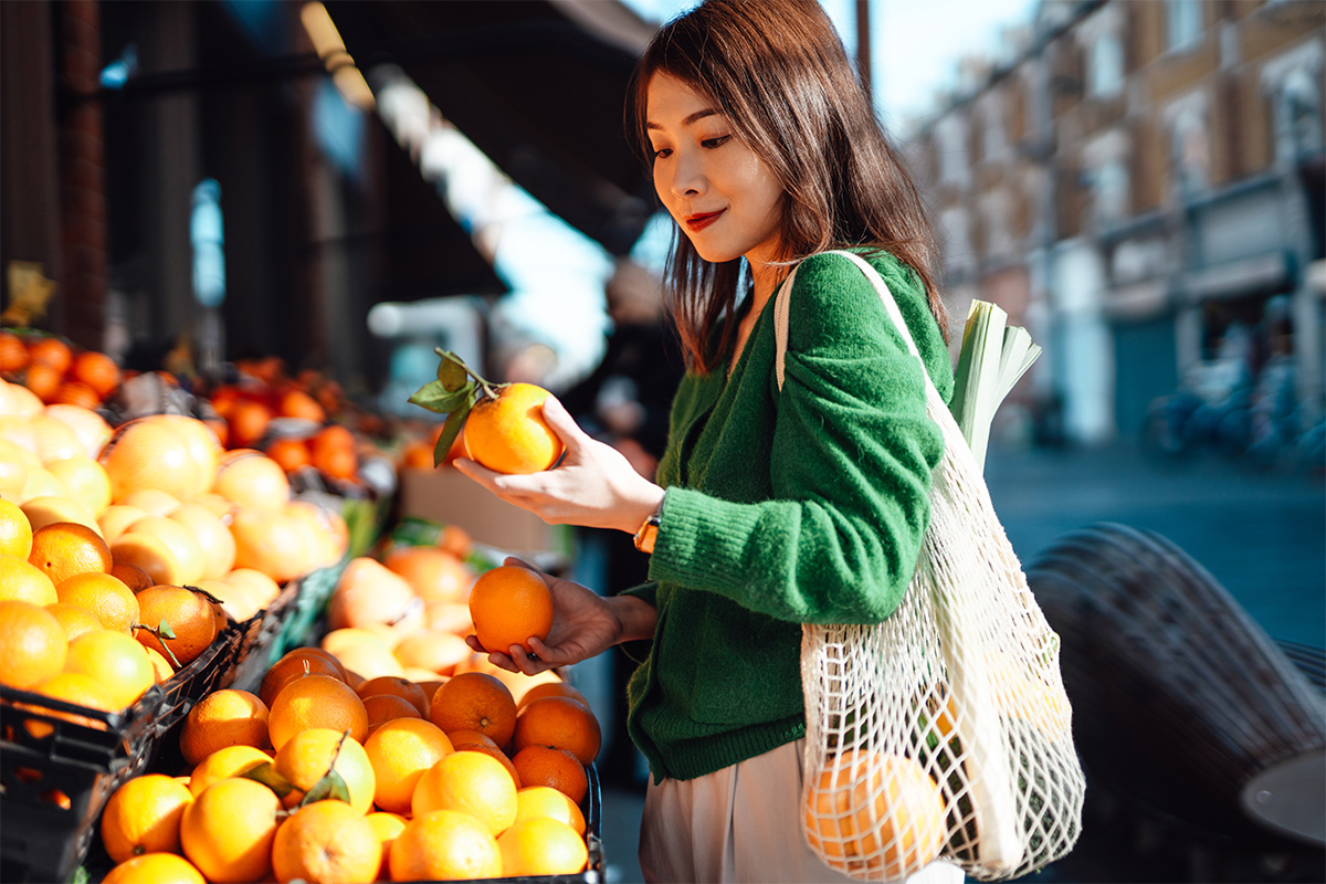 woman at fruit and veg market stall holding an orange 