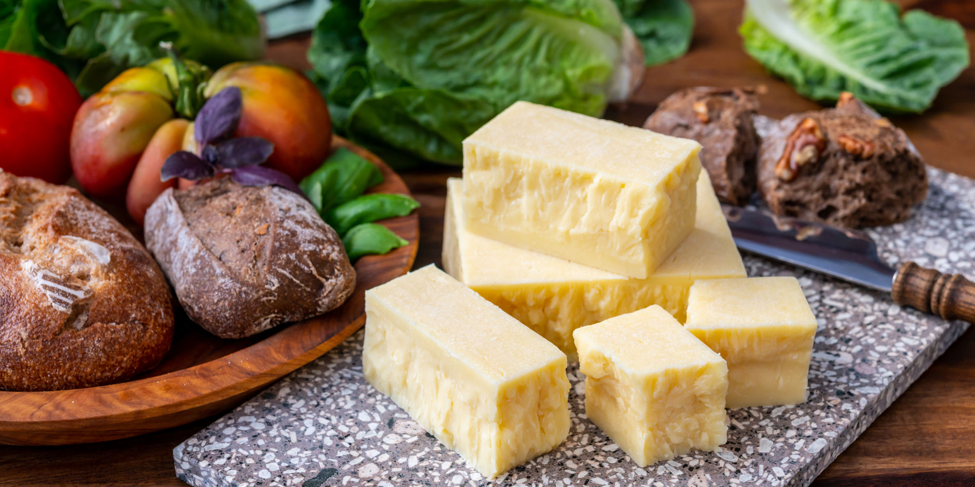 Blocks of cheddar on board next to bread and salad