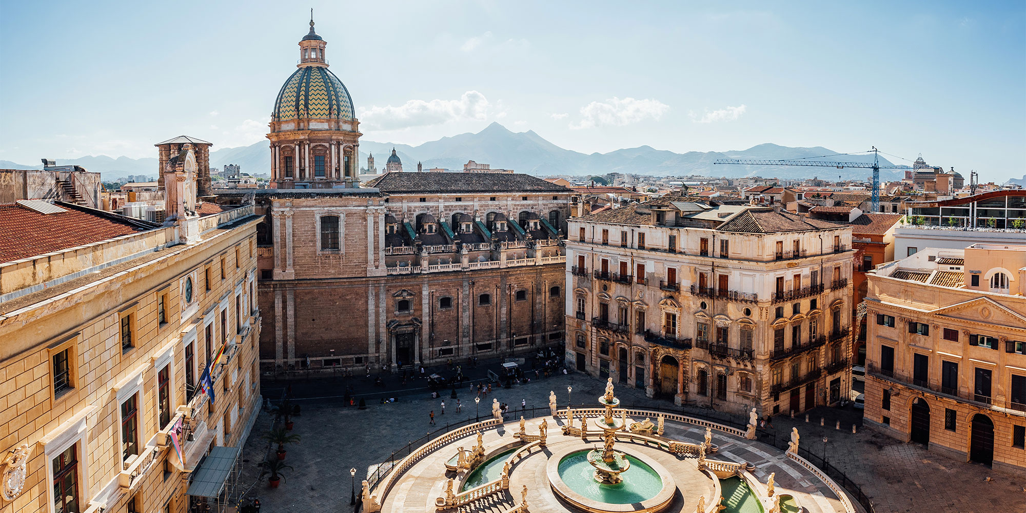 Aerial view of Palermo, Italy with its central fountain, surrounded by historic buildings and mountains in the distance.