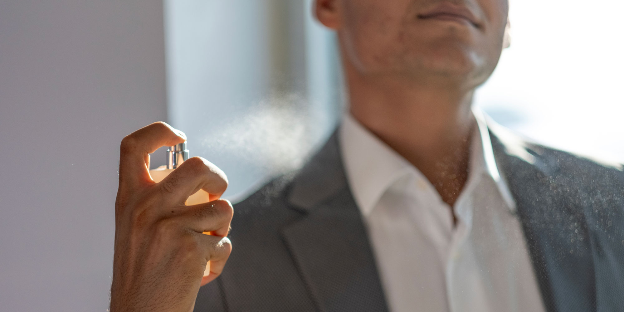 Men in grey suit spraying perfume on their neck