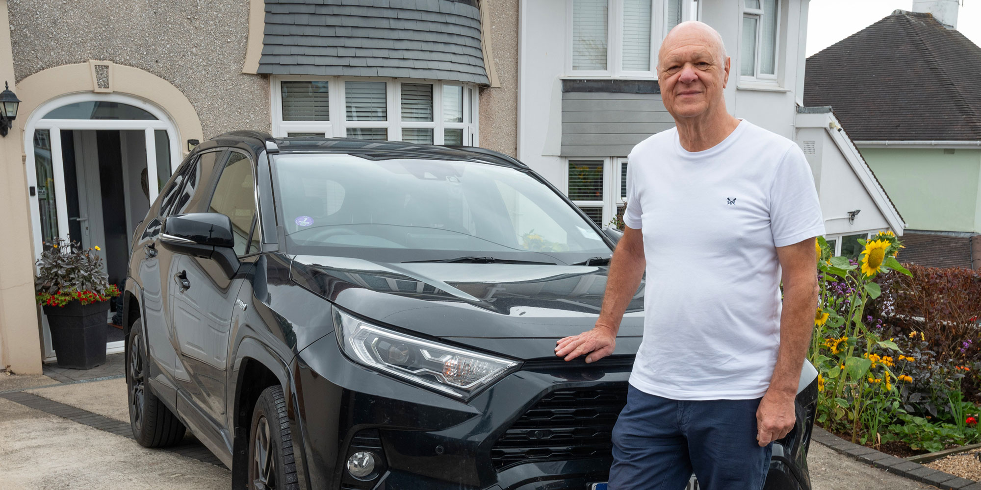 Man standing next to black Toyota Rav4, parked on a driveway.