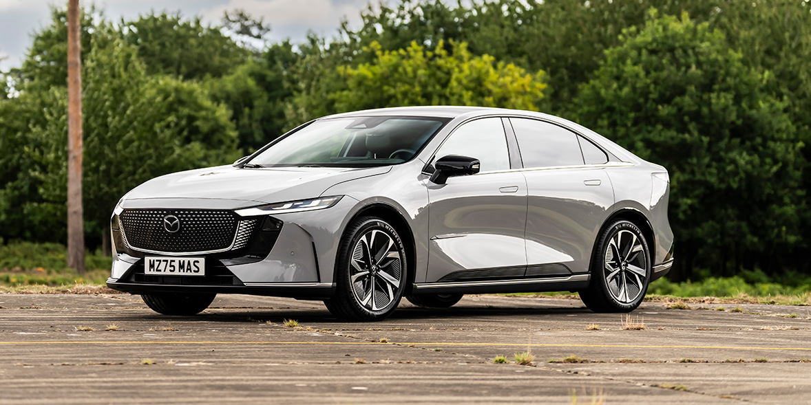 A grey Mazda 6e parked in front of some shrubs