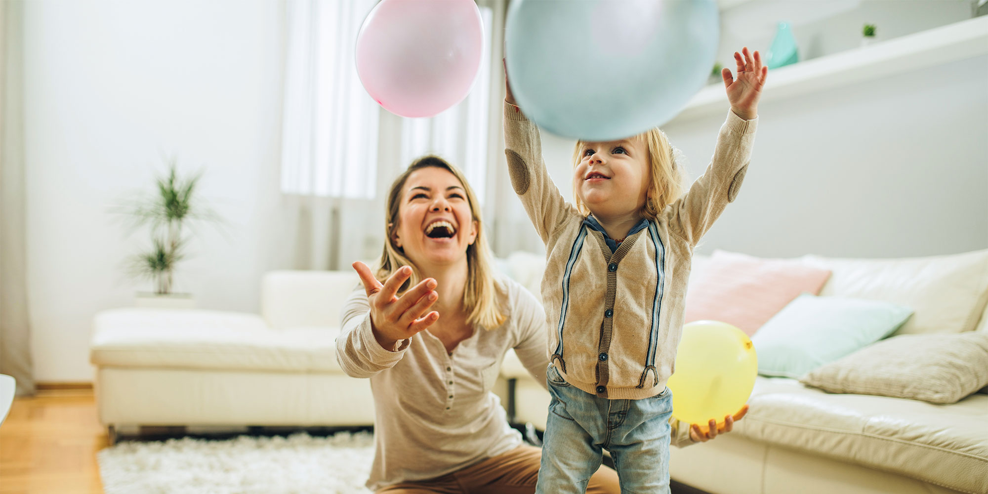 A woman and a child in a home setting playing with two balloons