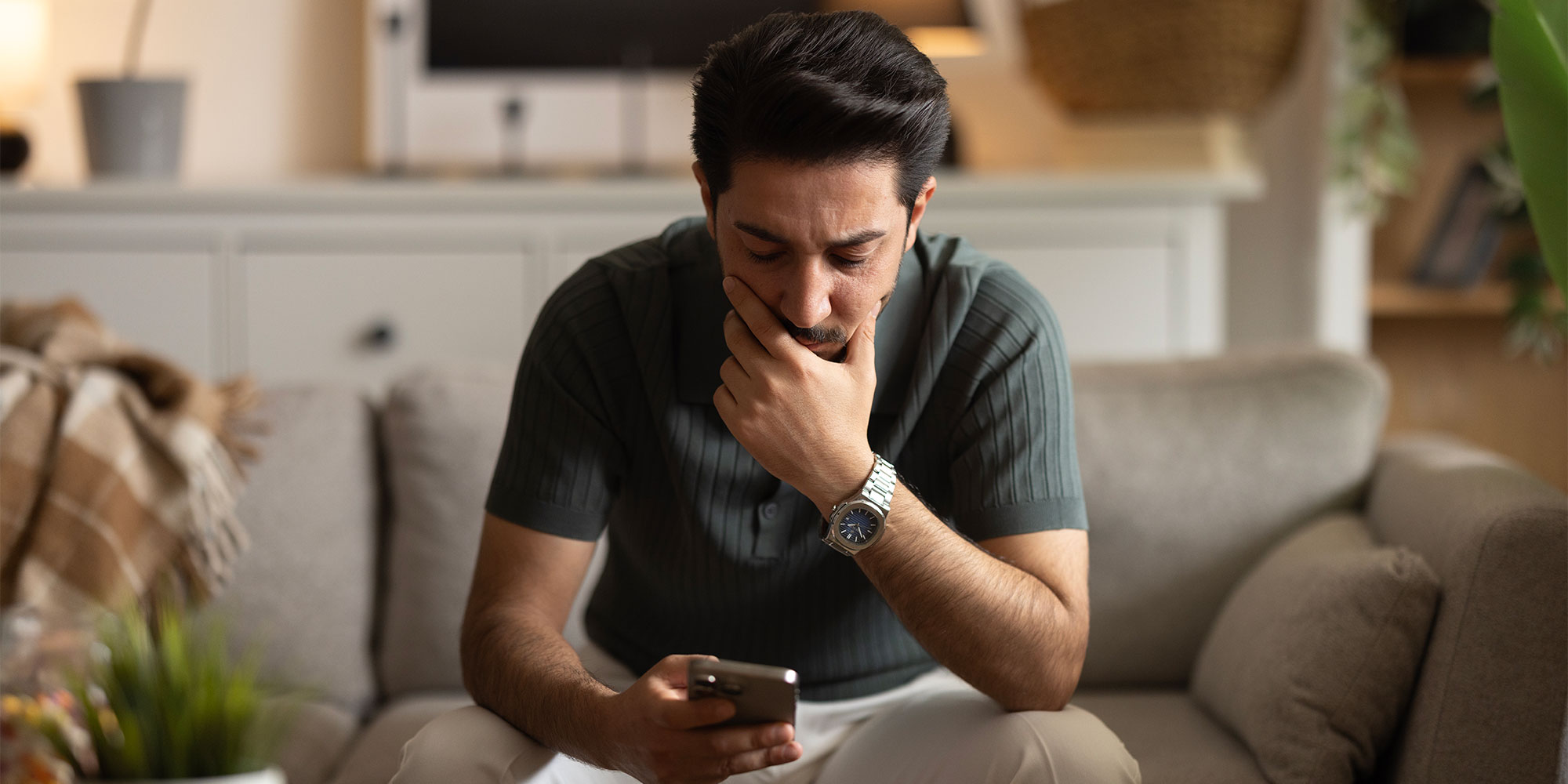 Dark-haired man looking at his phone pensively