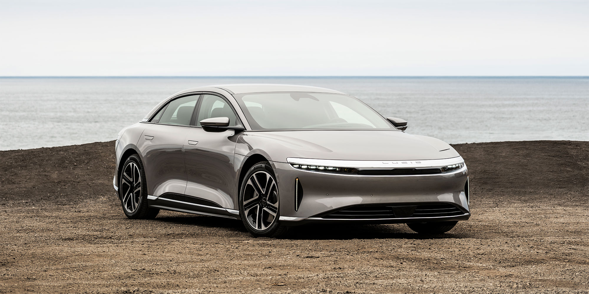 A grey Lucid Air is parked in front of a body of water