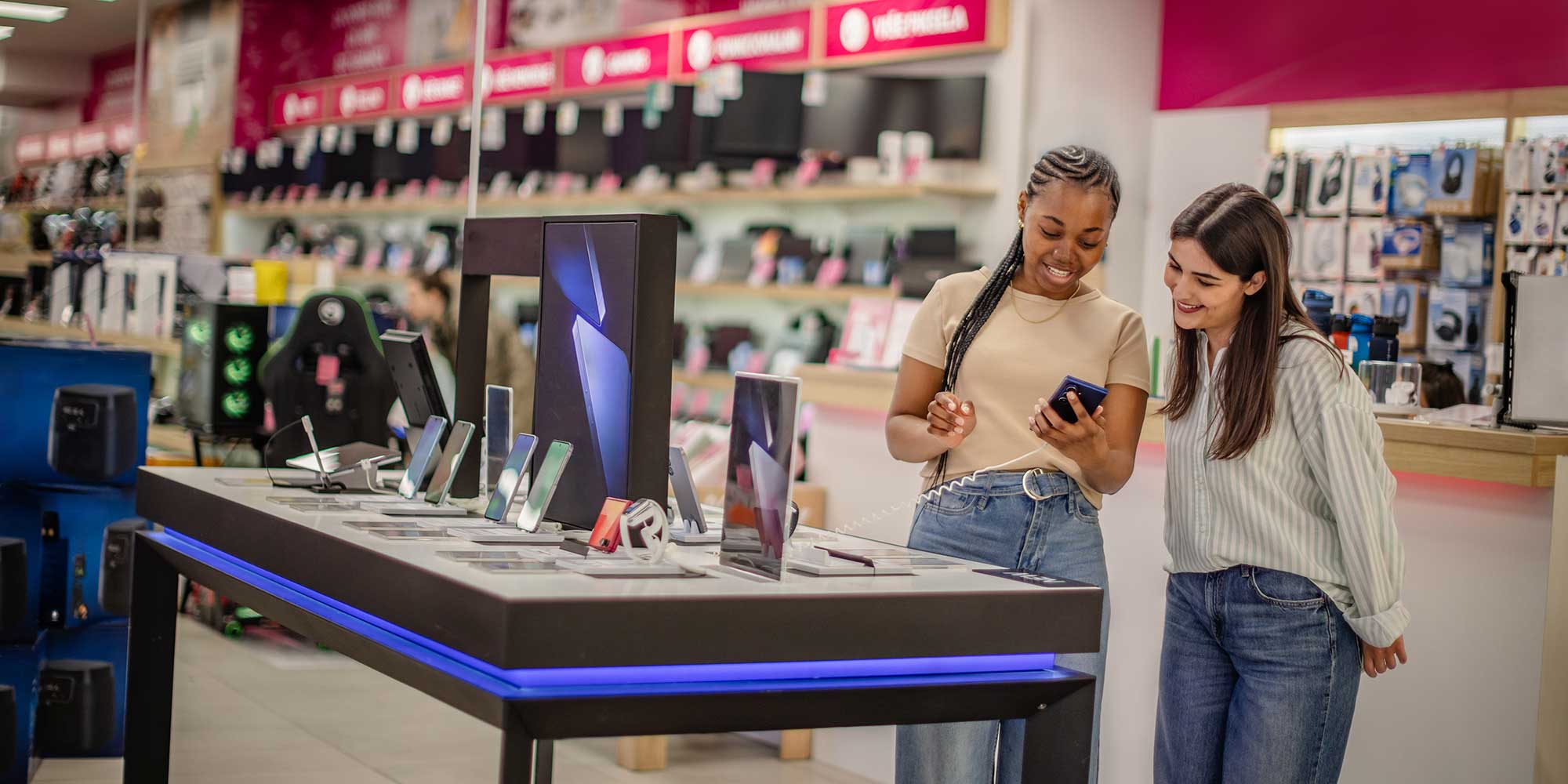 two women looking at phones in a tech store