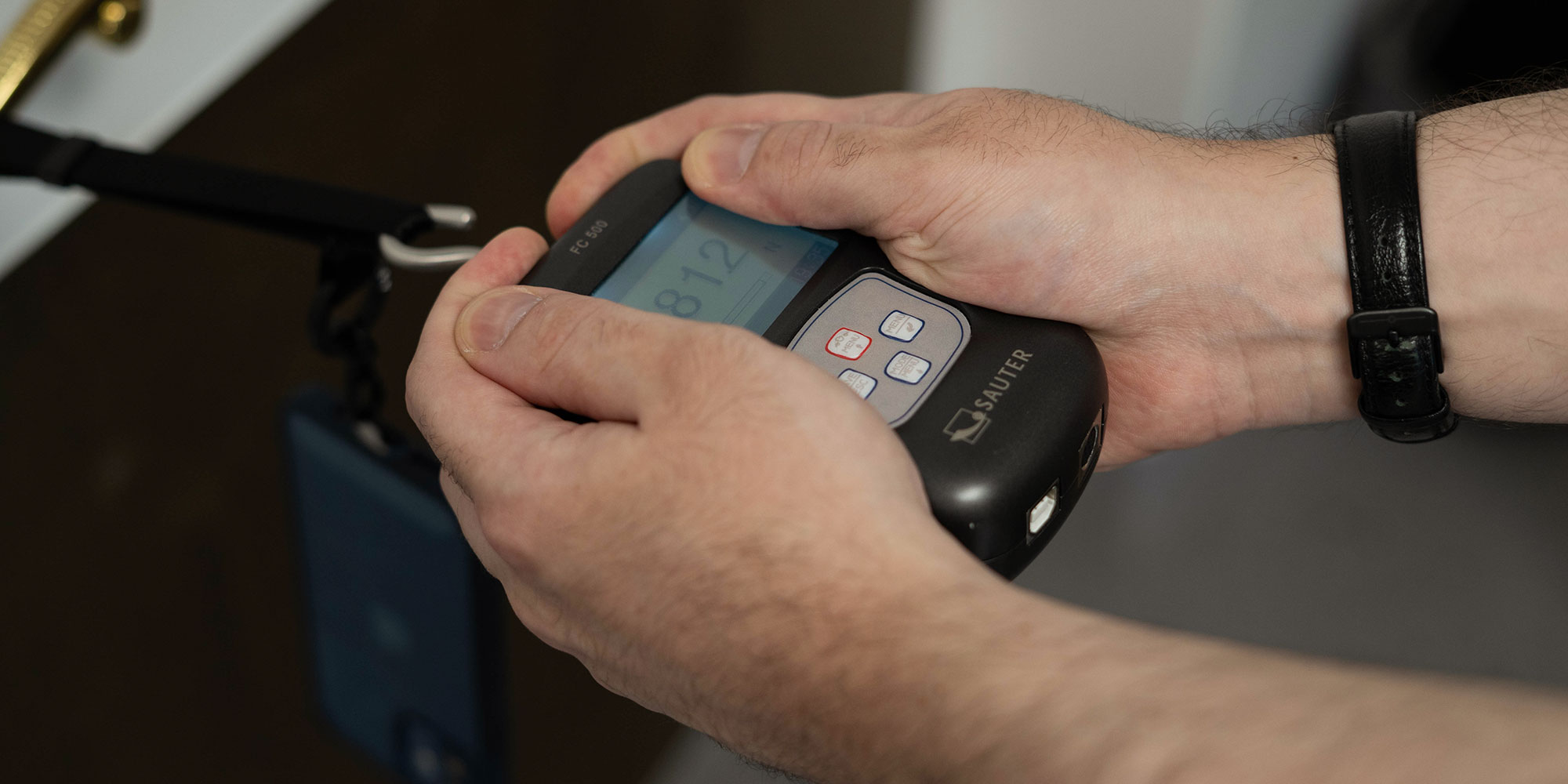 Mobile phone lanyard undergoing the force test while being measured by a Newton metre