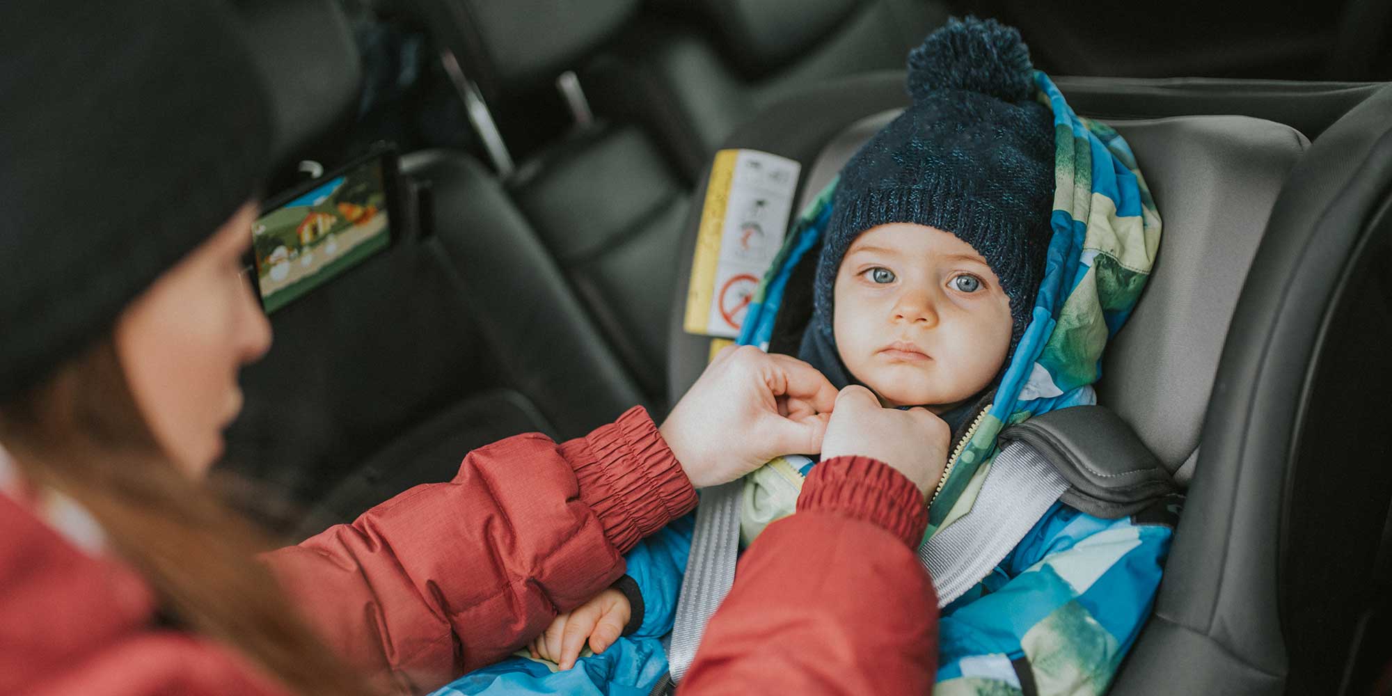Child in a puffy winter snowsuit being strapped into a car seat