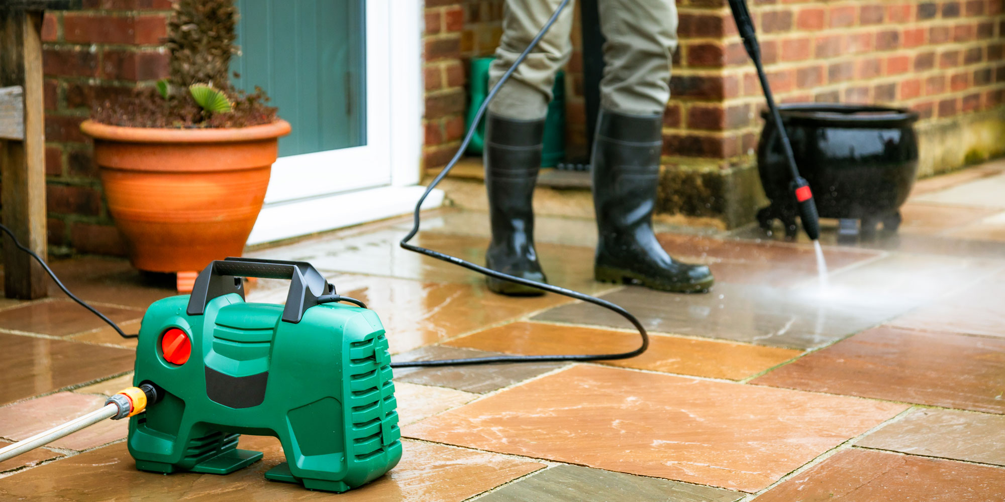 A person using a pressure washer to clean their garden patio