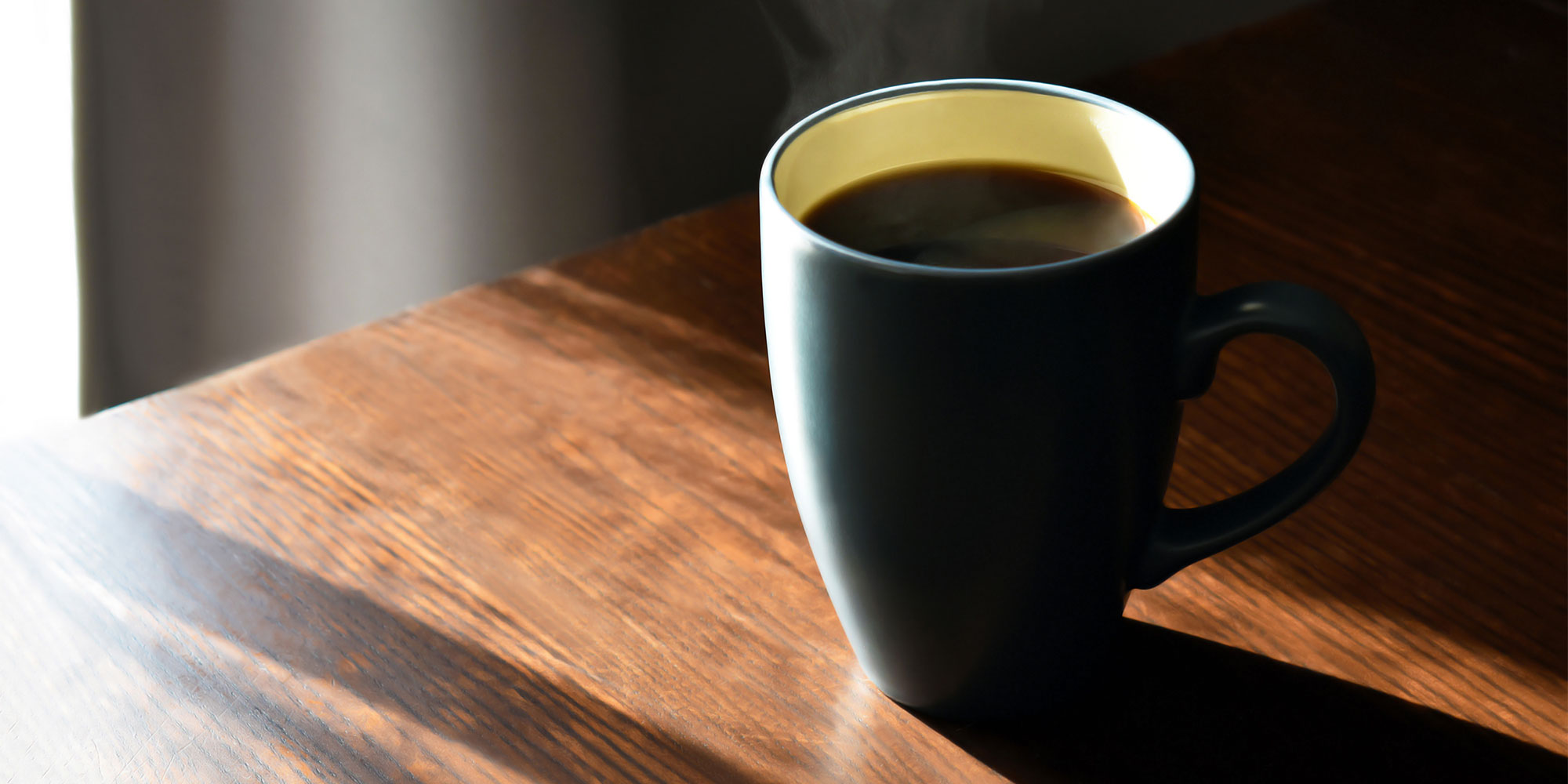 black coffee in a mug on wooden table with sunlight shining through