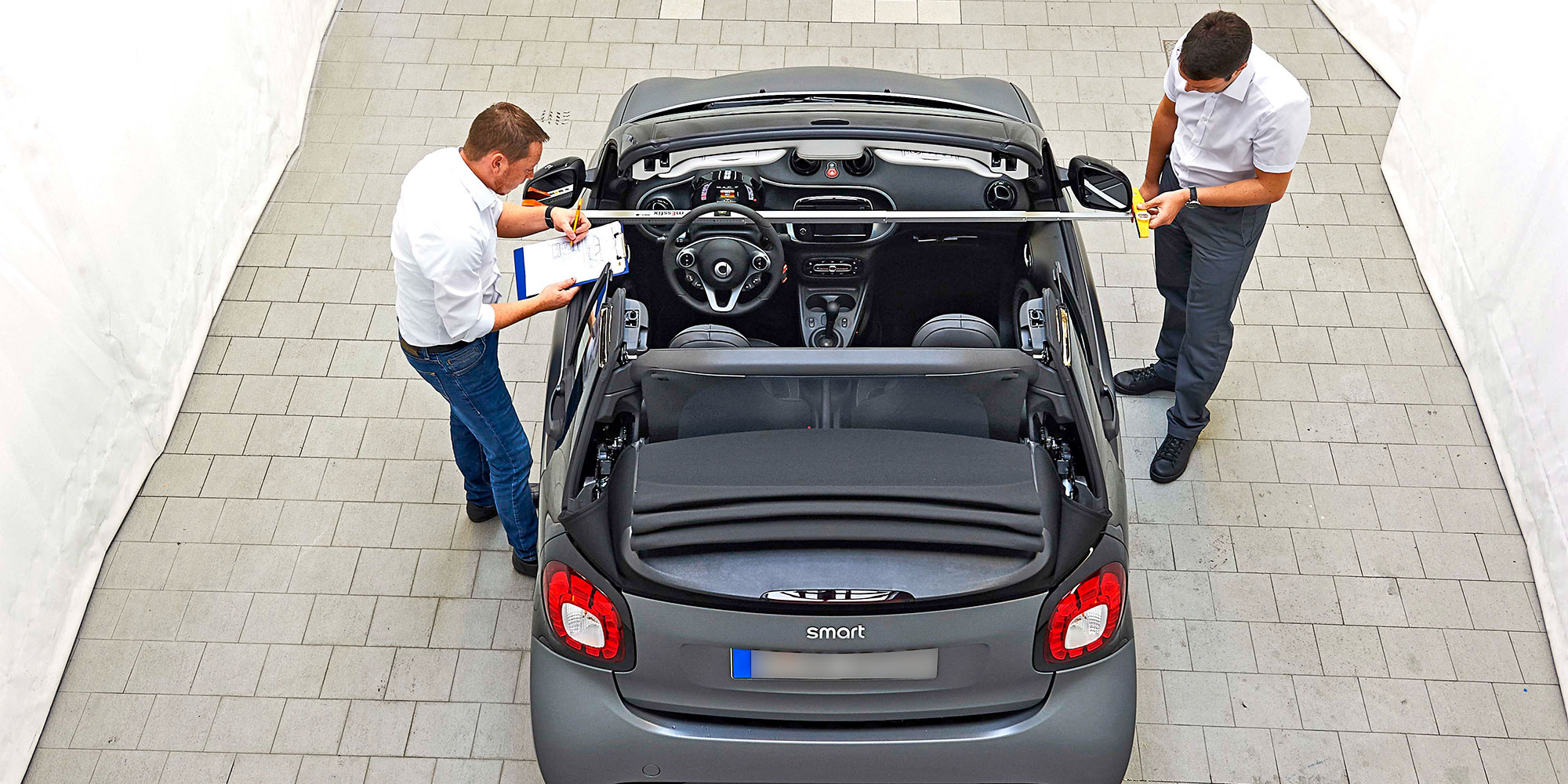 Two men measure the width of a Smart fortwo car.
