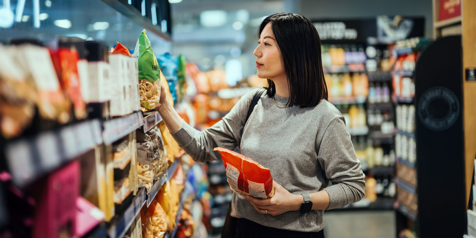 Someone choosing packets of crisps from a shelf display in a shop.
