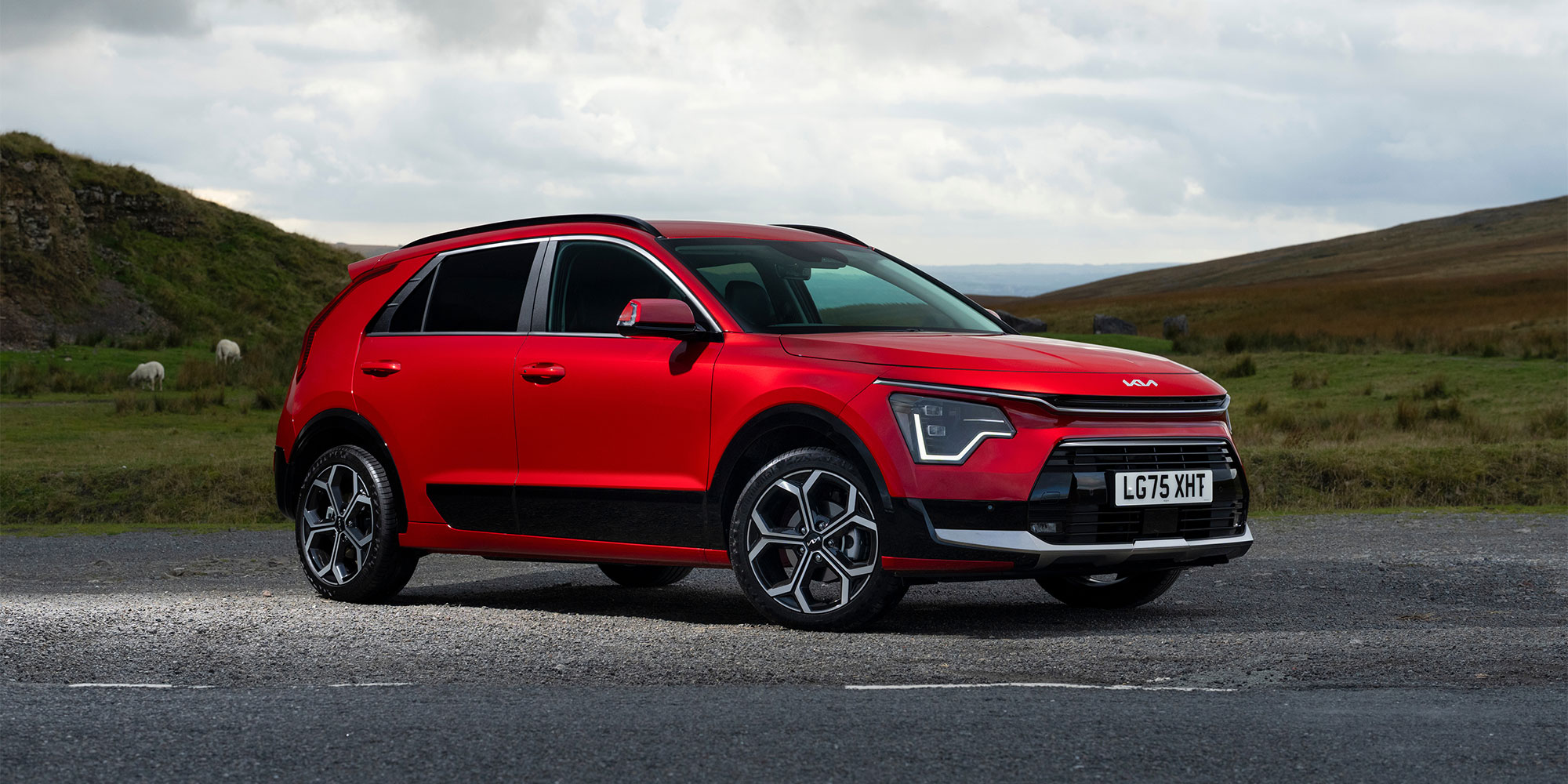 A red Kia Niro Hybrid, parked in a rural setting