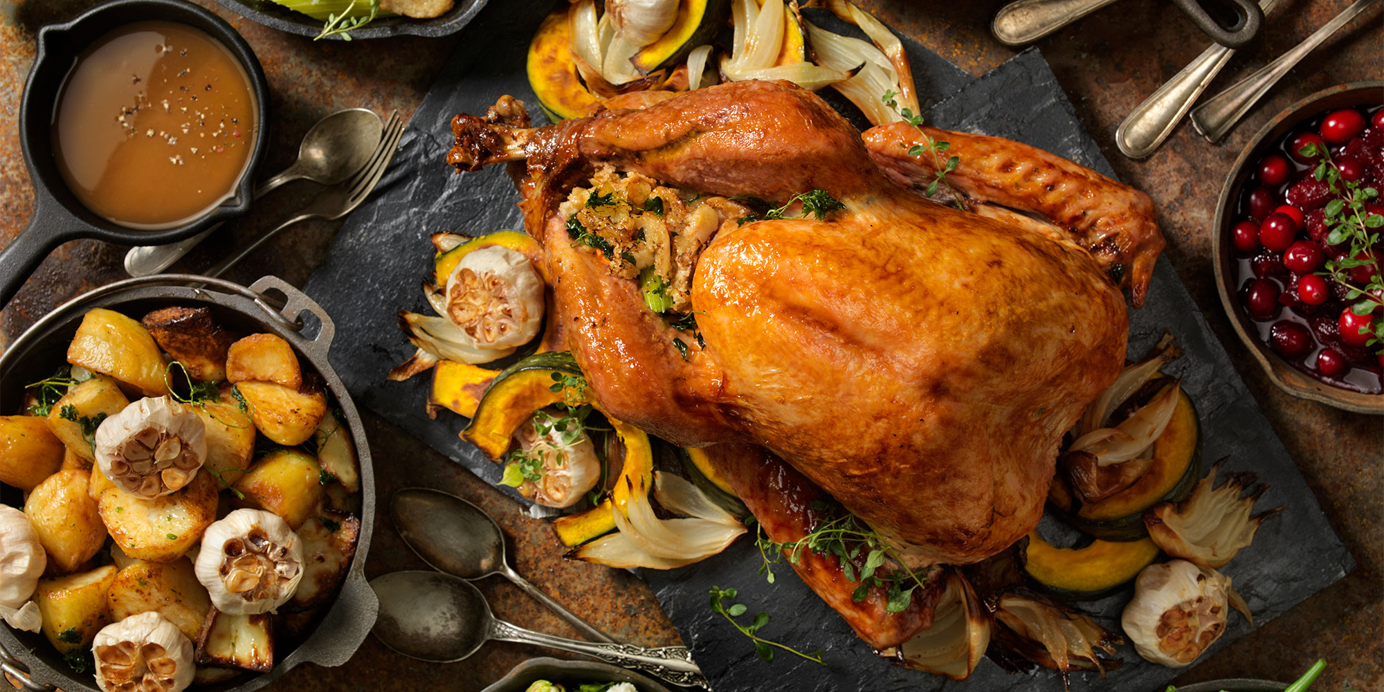 Roasted turkey on a platter with roasted vegetables, potatoes, and cranberry sauce on the side.