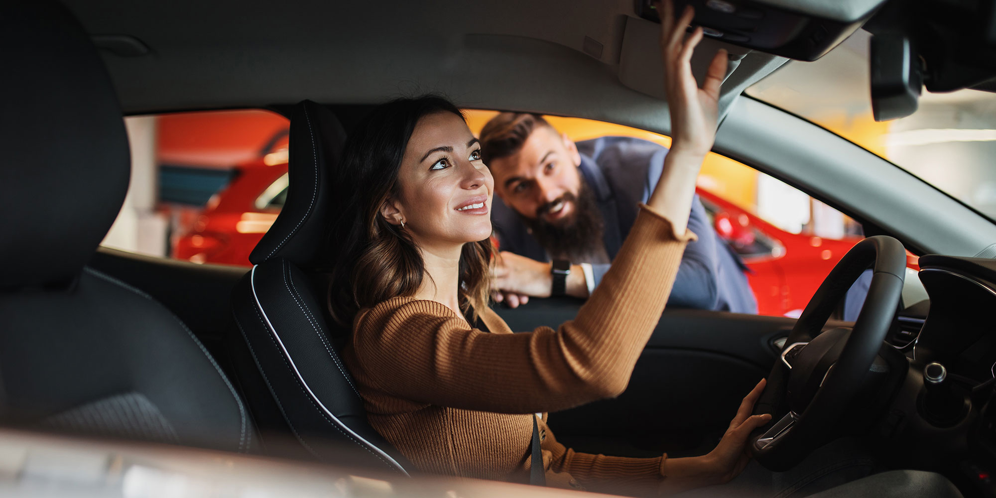 A woman sitting in a car with the car salesperson leaning in on the car window, showing her the car