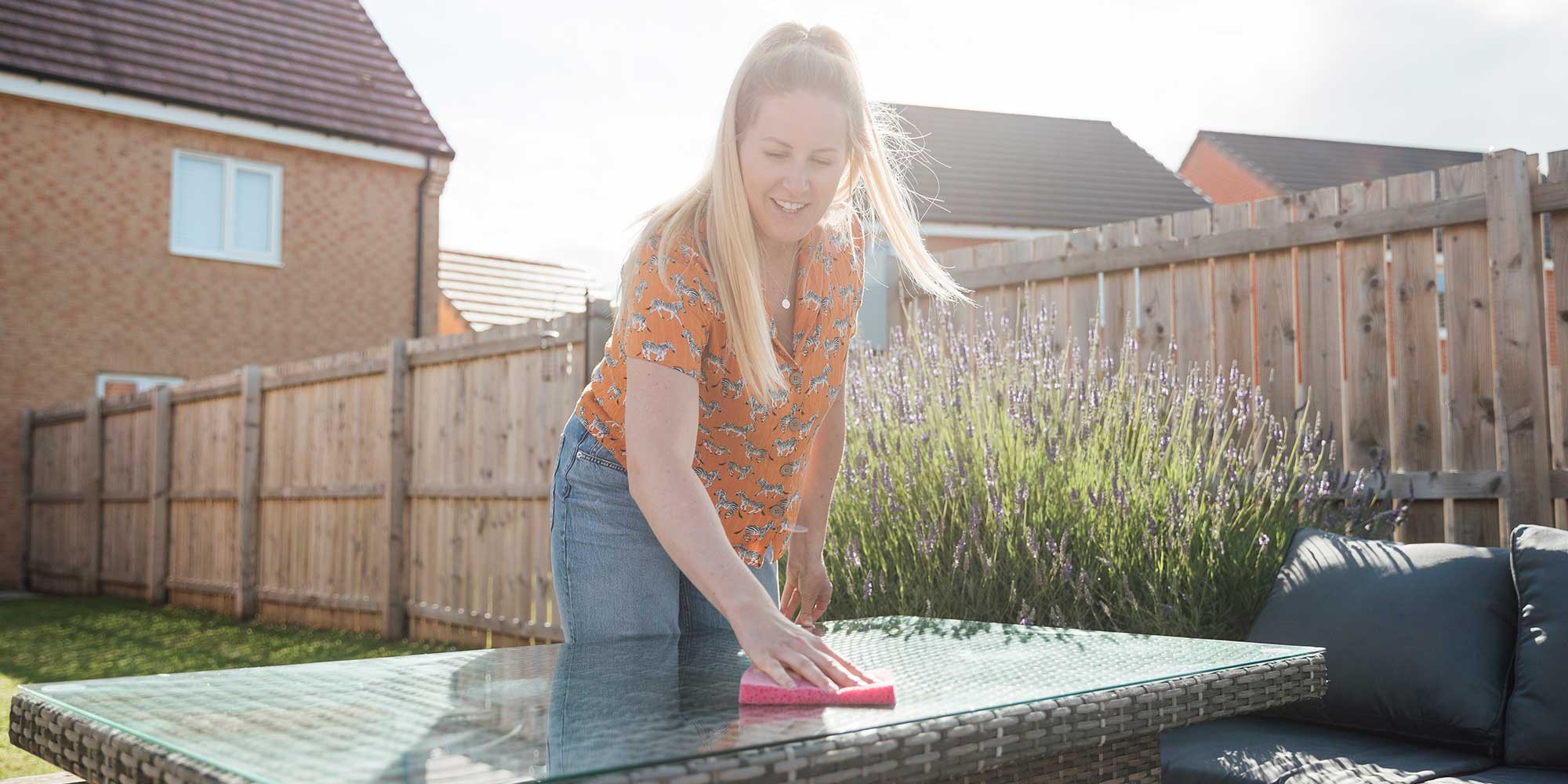A woman cleaning a glass garden table with a pink cloth.