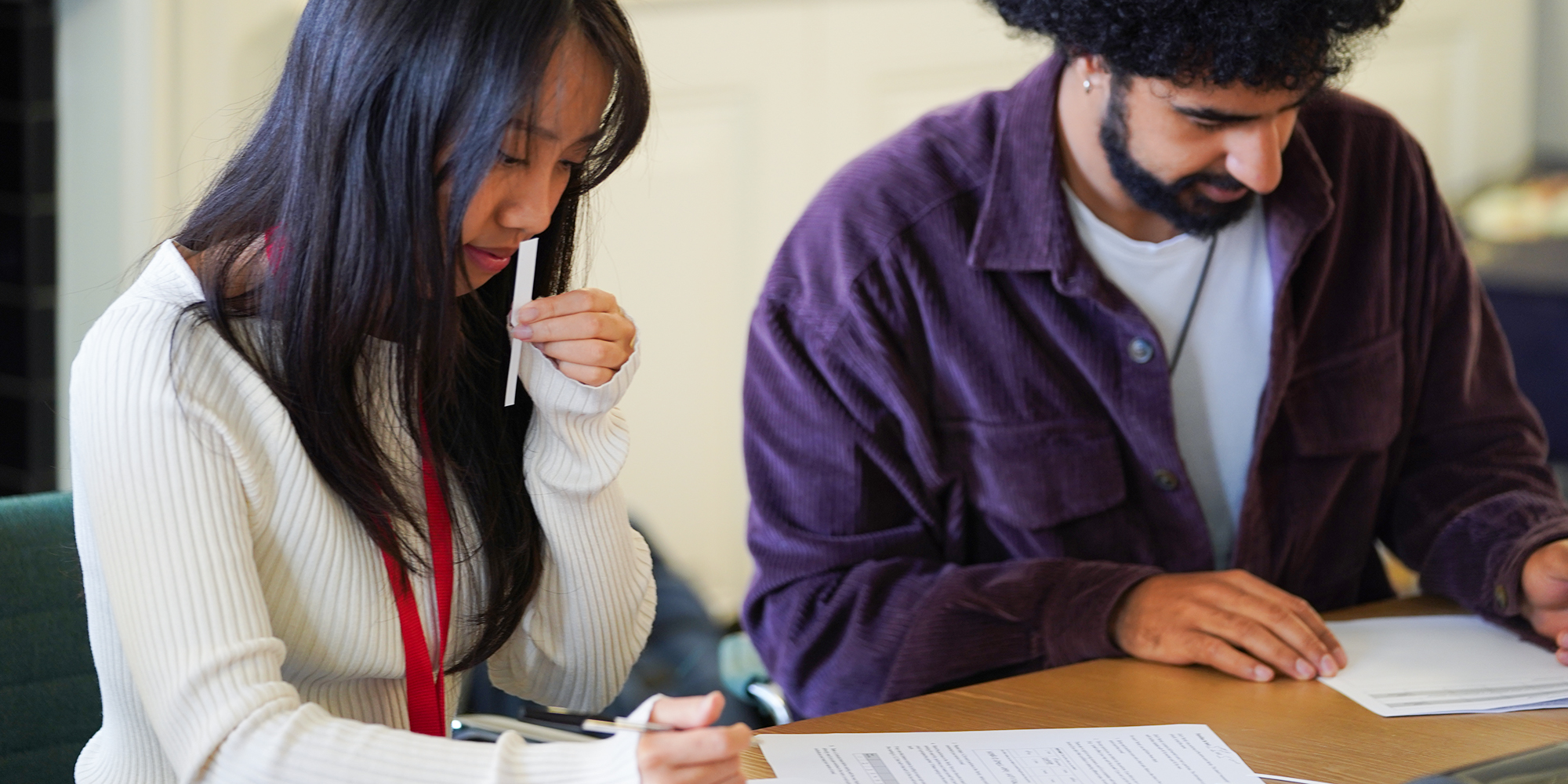 Woman in white jumper smelling a perfume and man in purple shirt writing on paper - Which? perfume expert test