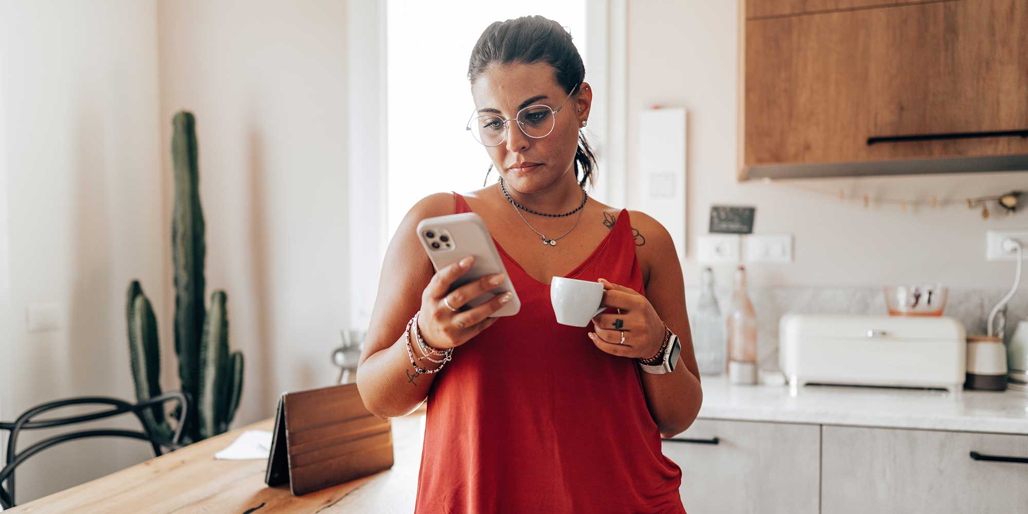 A woman holding a cup in her hand while looking at her mobile phone in her other hand