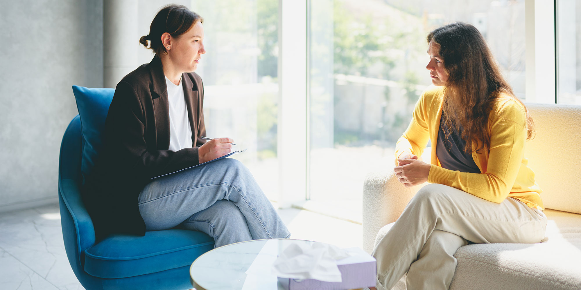Two women sat having a conversation, one holding a clipboard