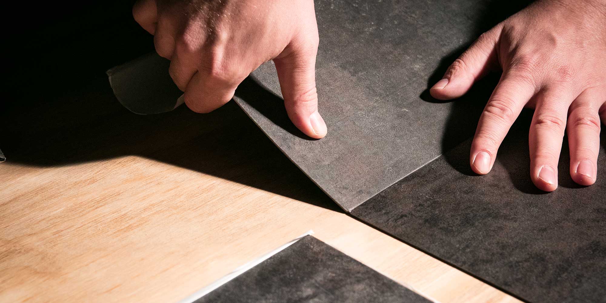 Person sticking down self-adhesive floor tiles