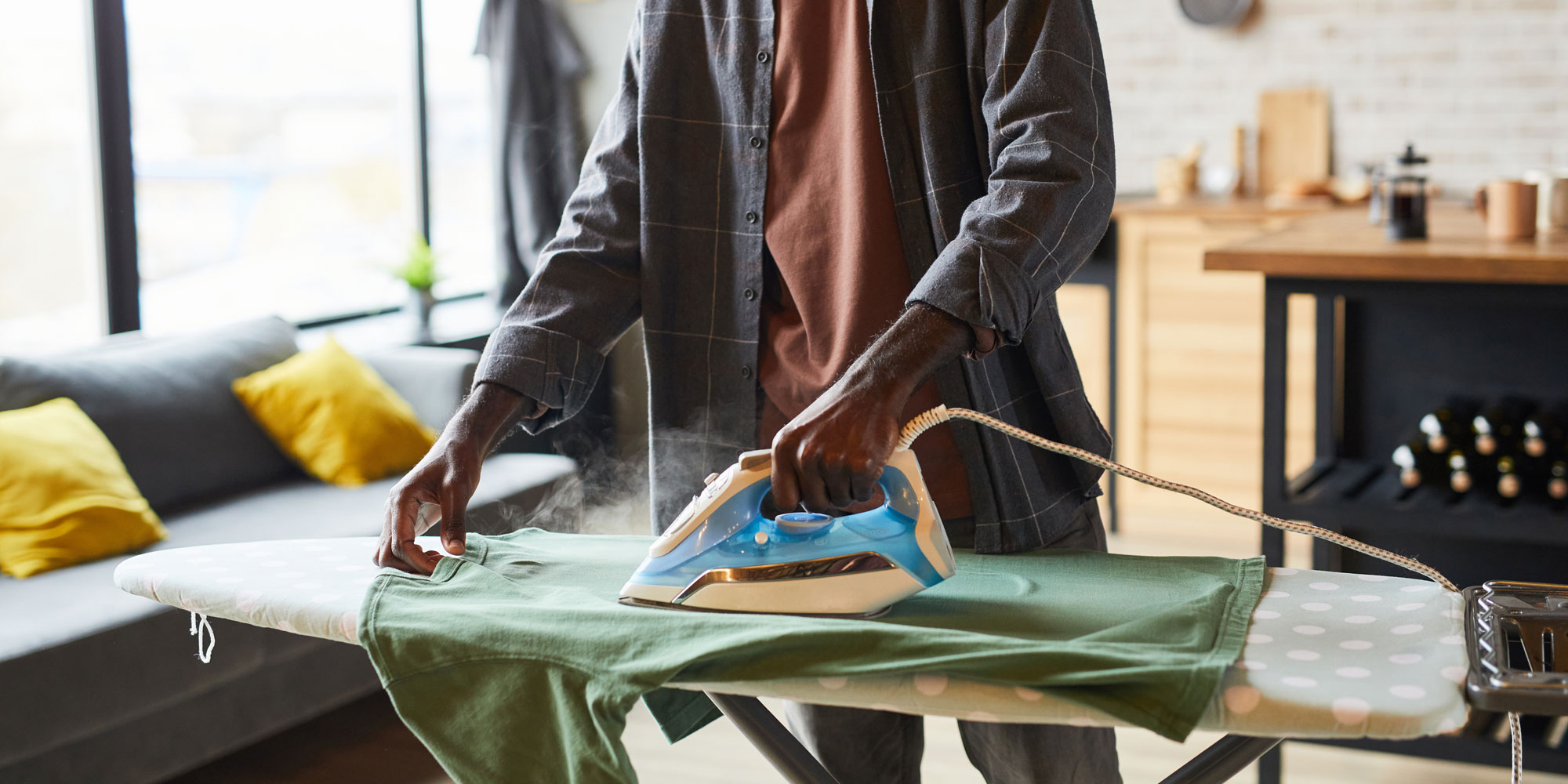 person ironing a green shirt with a steam iron