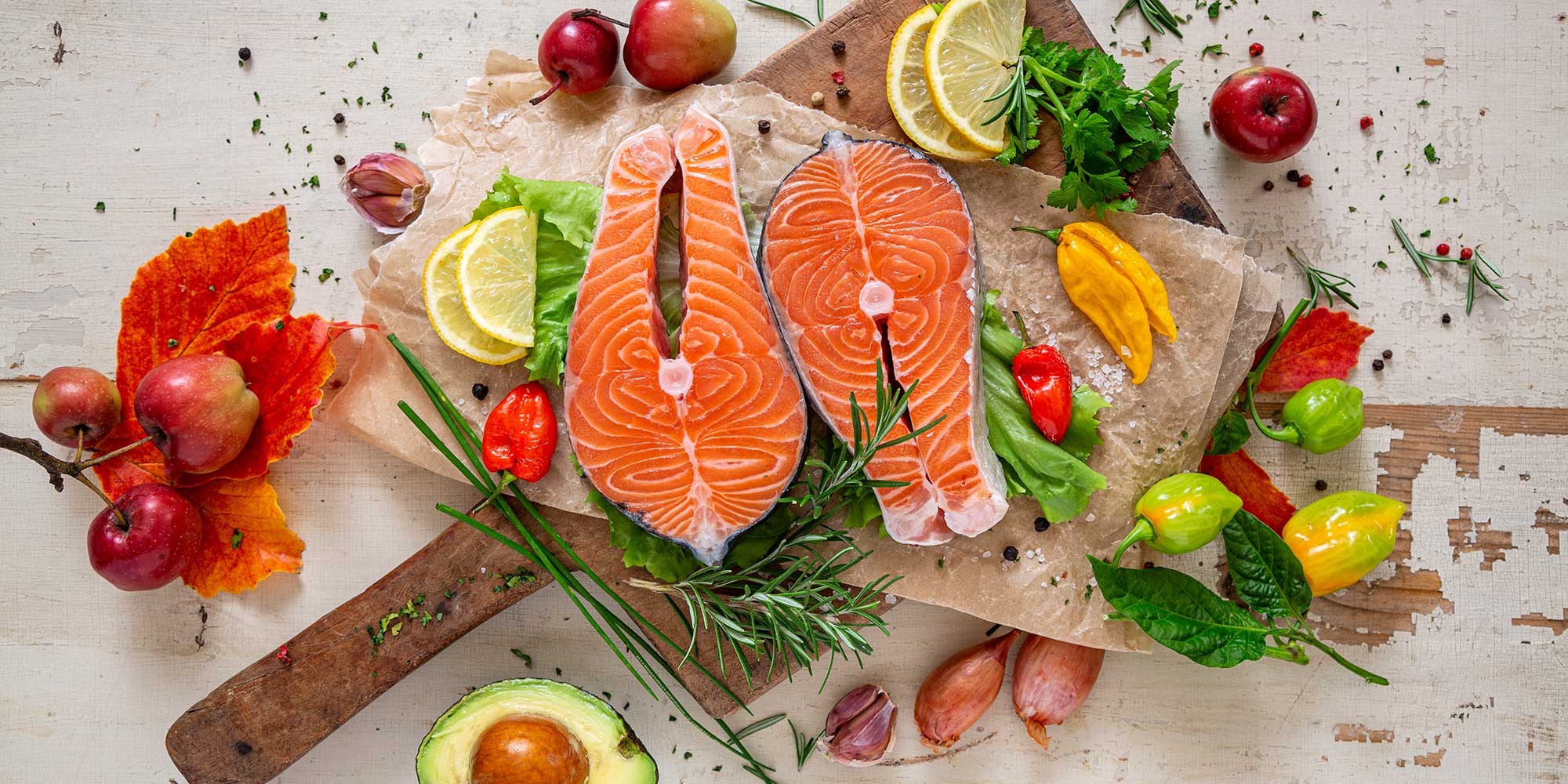 Raw fish on a chopping board surrounded by fruit and vegetables
