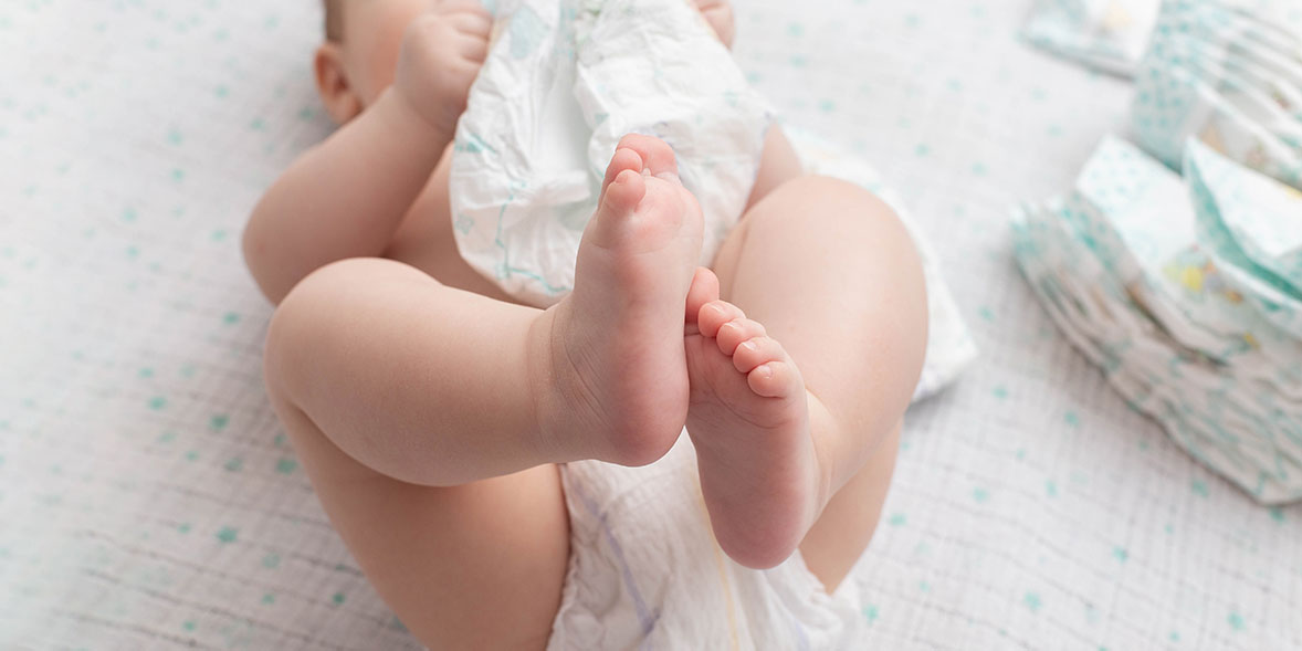 Baby wearing a nappy with a pile of nappies next to them