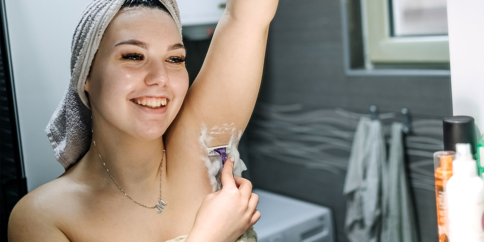 women in bathroom with towel on her head shaving armpit