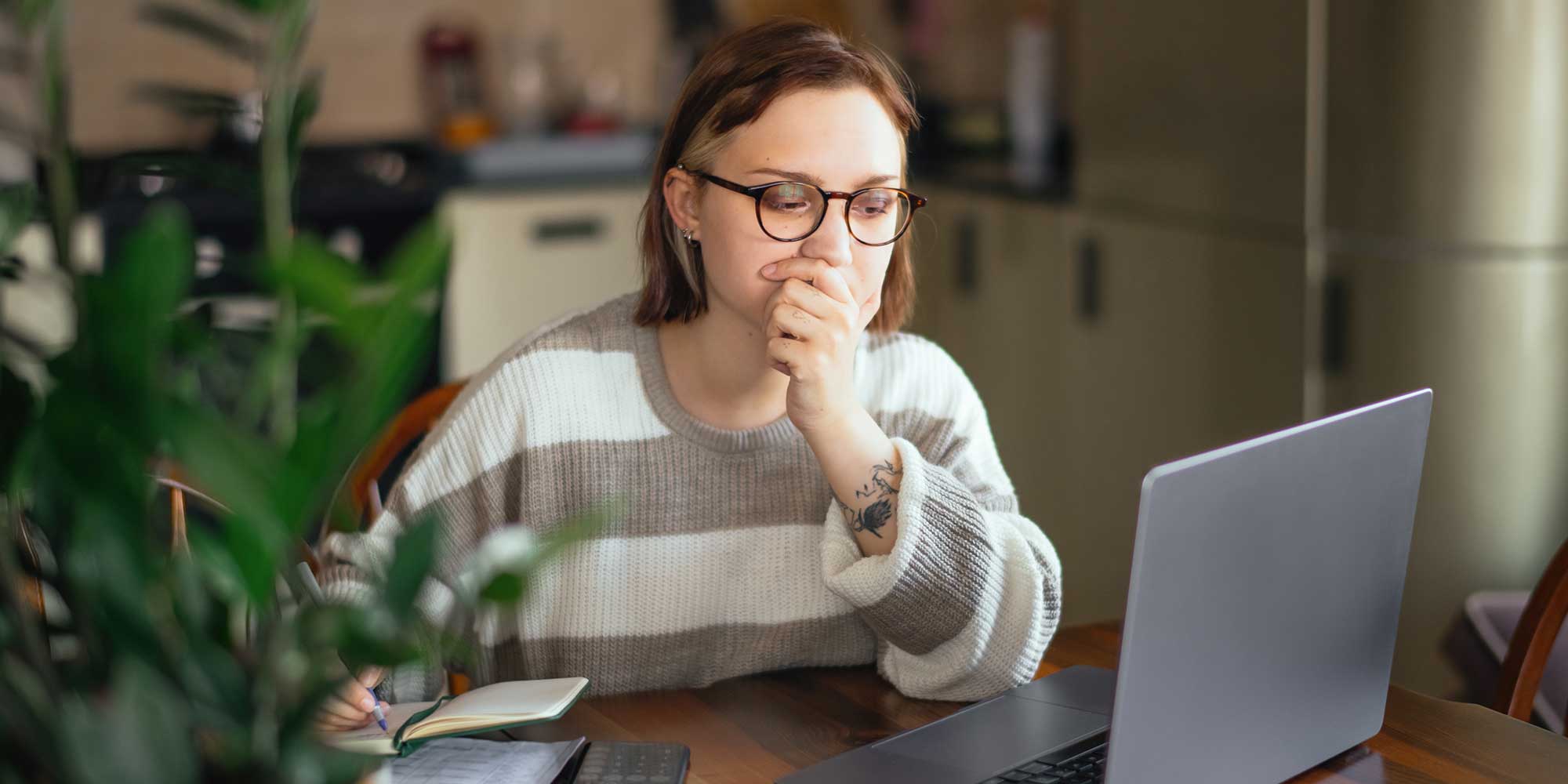 Woman in glasses and striped jumper looking worried at her laptop