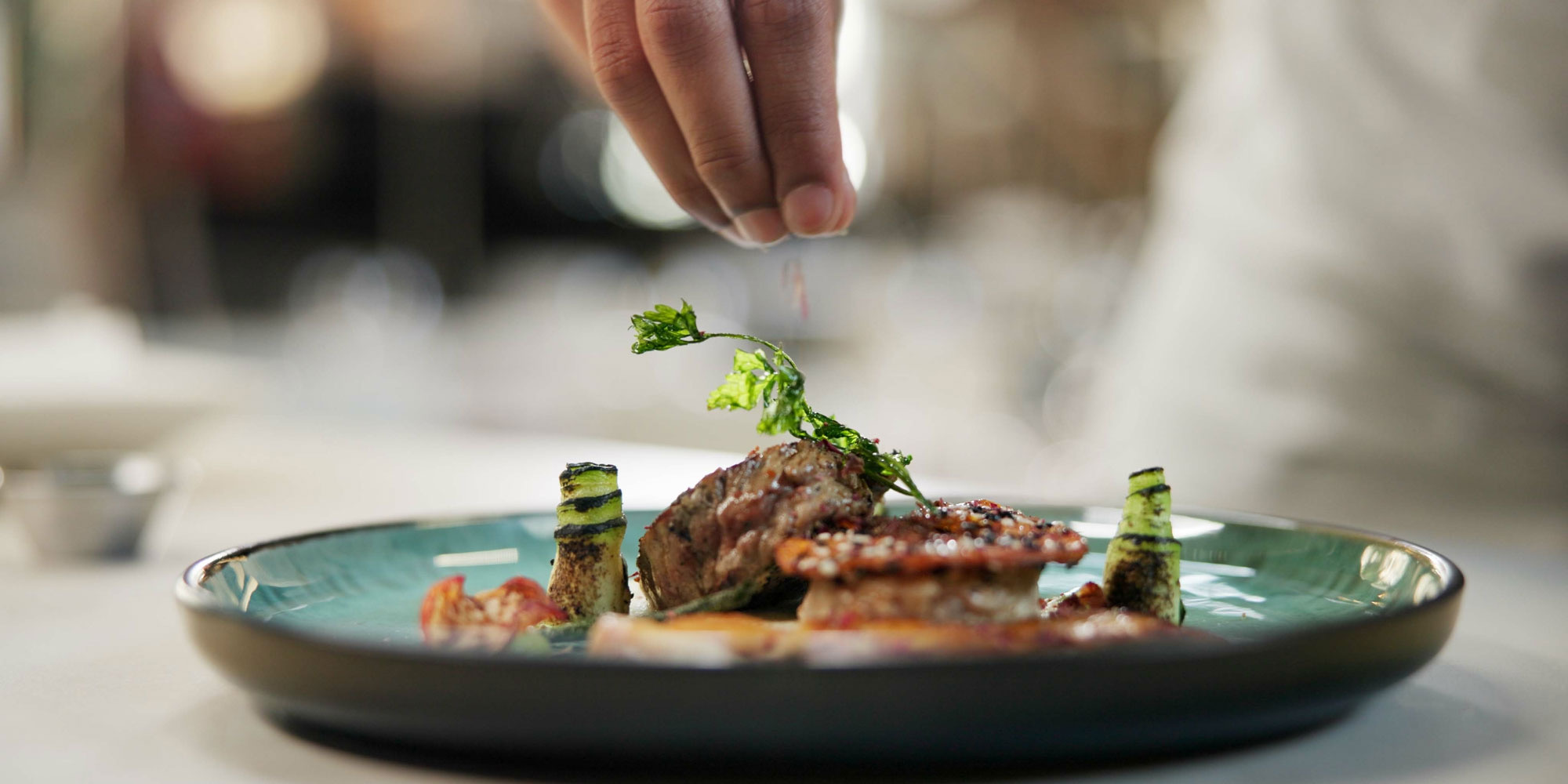 A chef places a garnish on a small plate of gourmet food