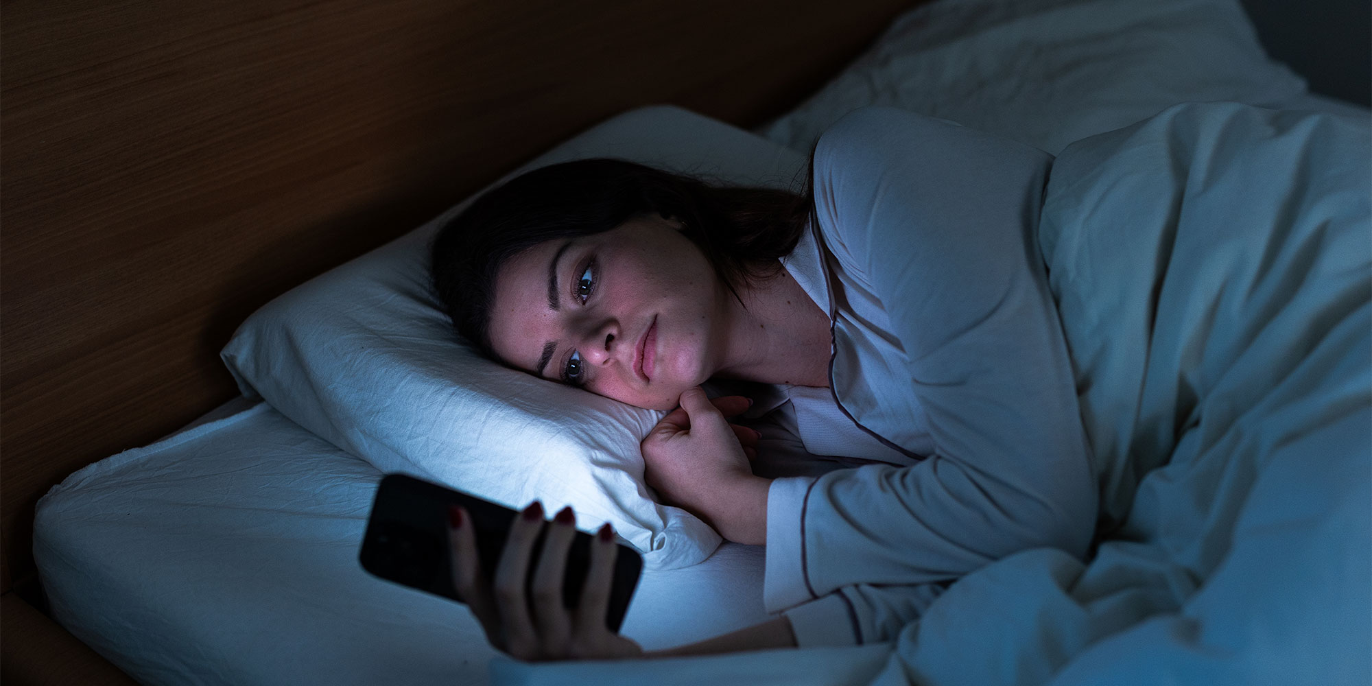 A woman lying in bed awake looking at her phone