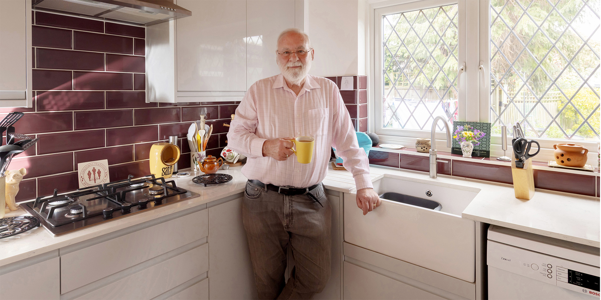 man drinking coffee in howdens kitchen with butlers sink and burgundy wall tiles  