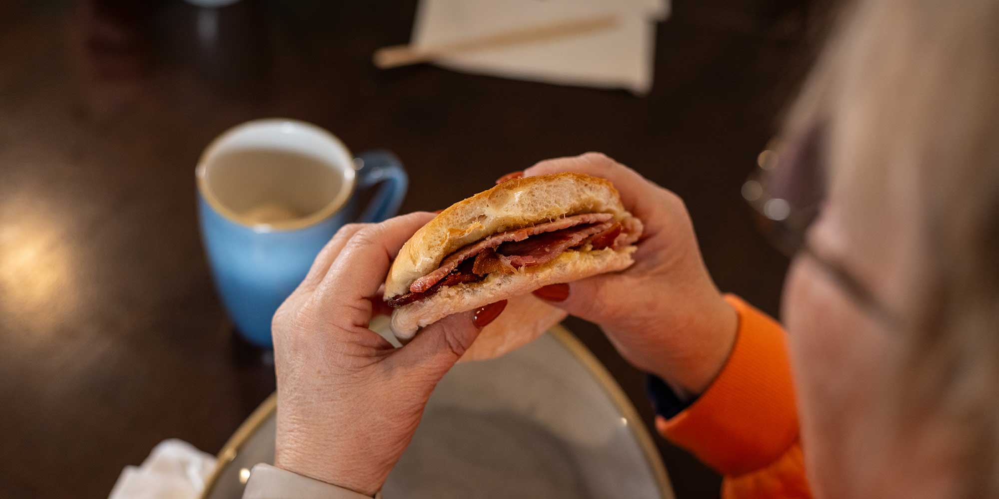 Someone holding a bacon roll, which they've eaten some of already.