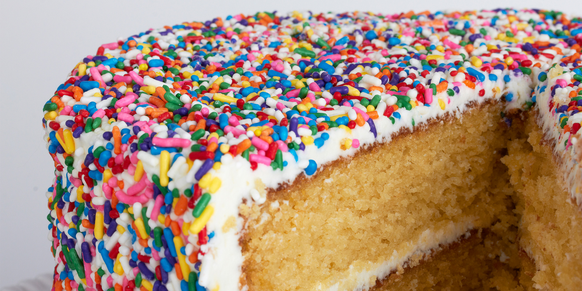 A cake covered in multicoloured sprinkles, with a slice cut out so you can see the centre.