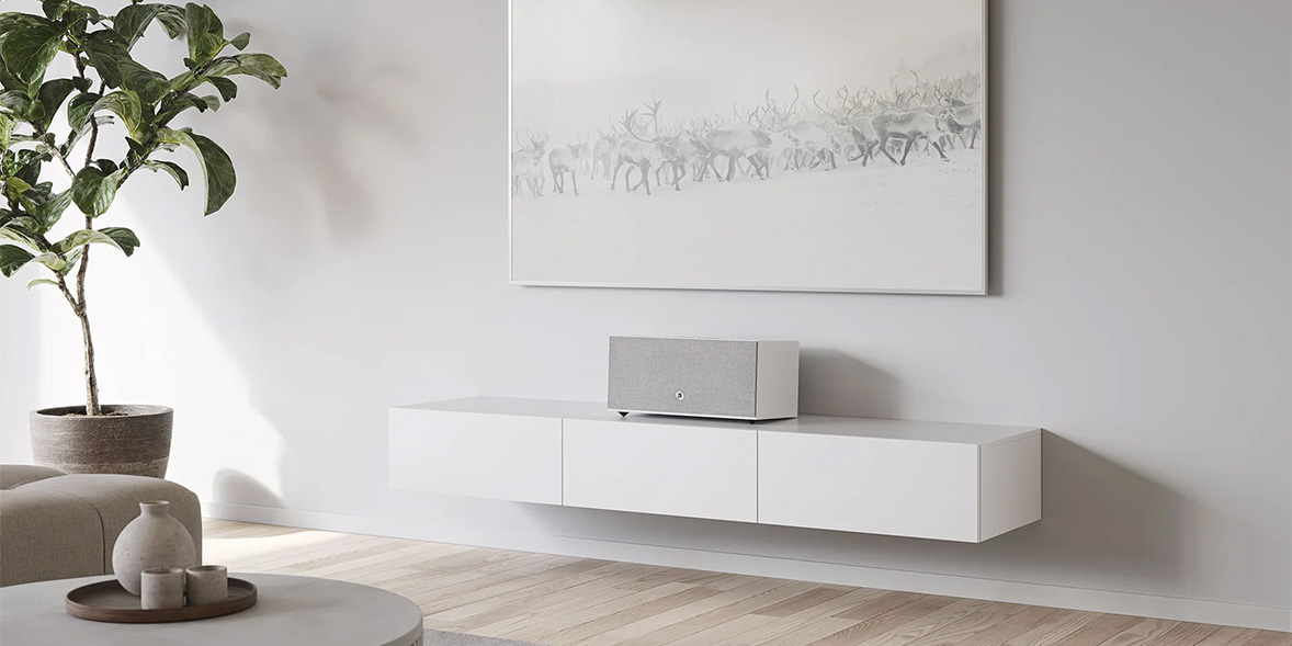 White living room with wall-mounted cabinet, speaker, art, and potted plant.