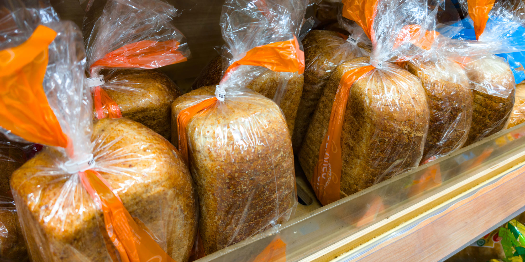 Loaves of sliced brown bread on a supermarket shelf, wrapped in plastic.