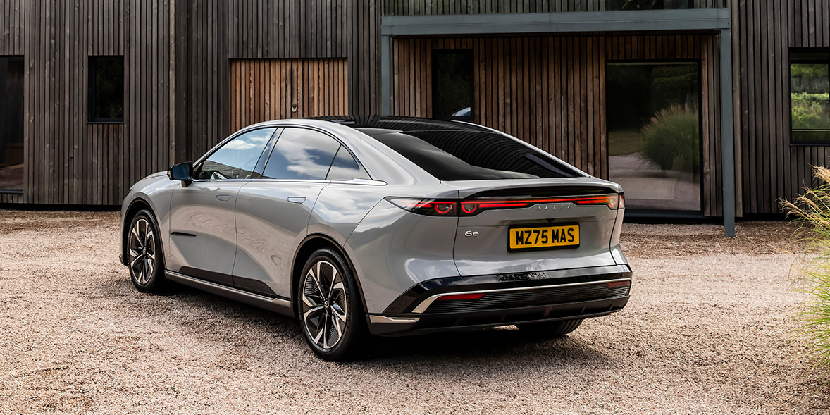 The rear of a grey Mazda 6e parked against a wooden building