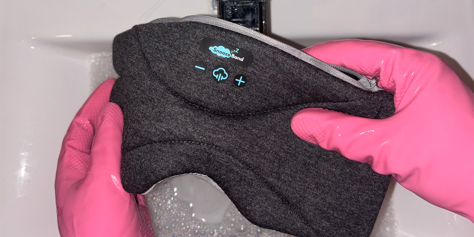 Someone washing a Bluetooth sleep mask in a sink with pink gloves