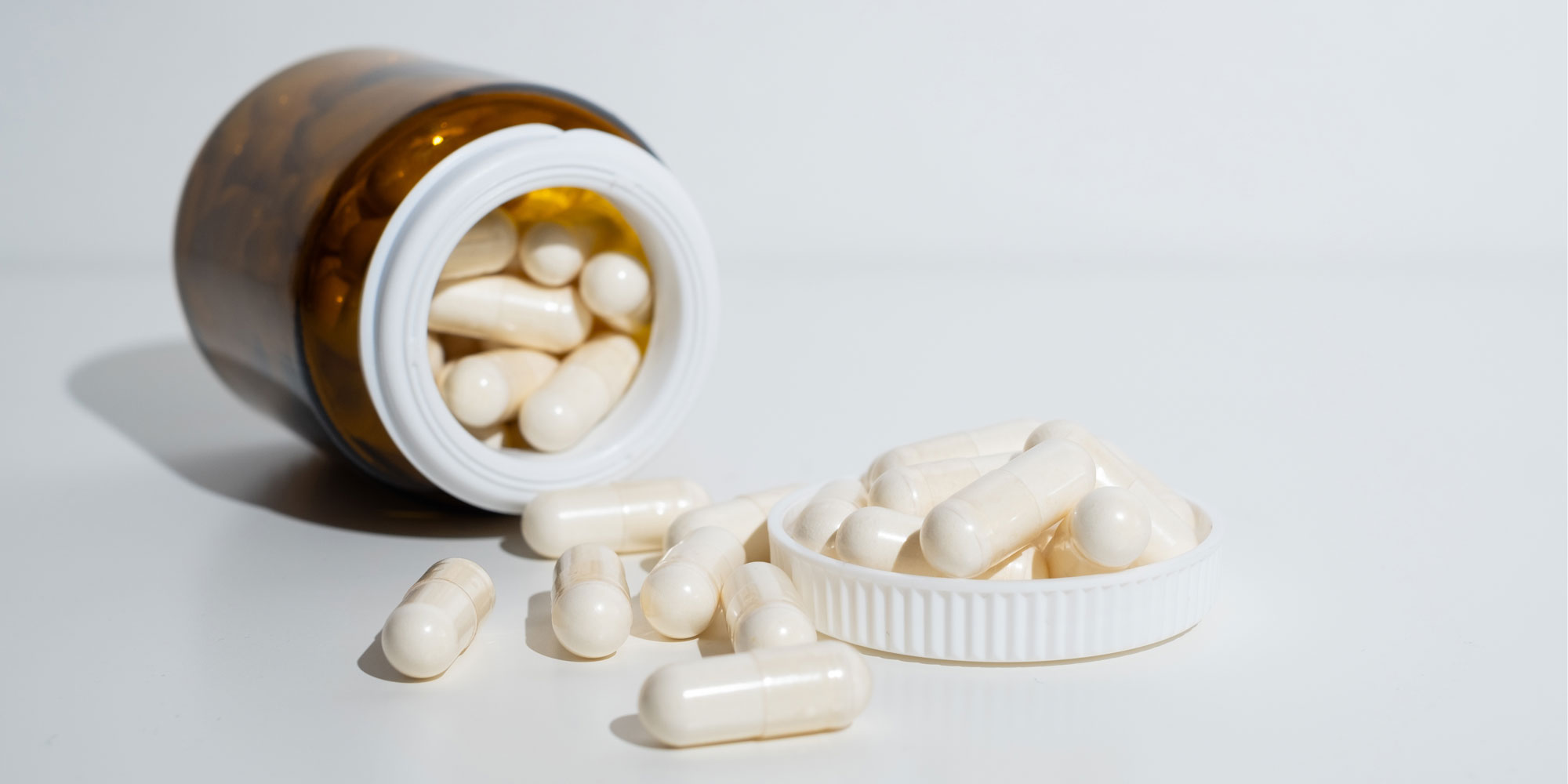 An open bottle of collagen pills lying on it's side. The pills are spilling out of the bottle. 