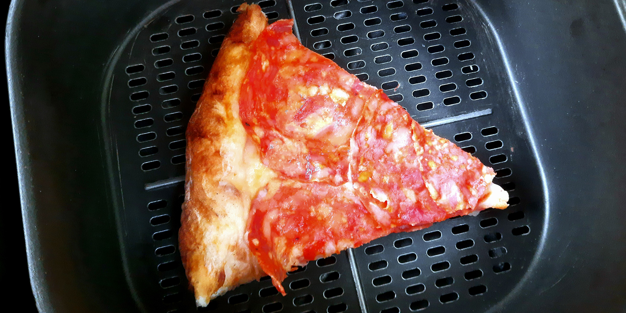 a slice of pepperoni pizza in an air fryer basket