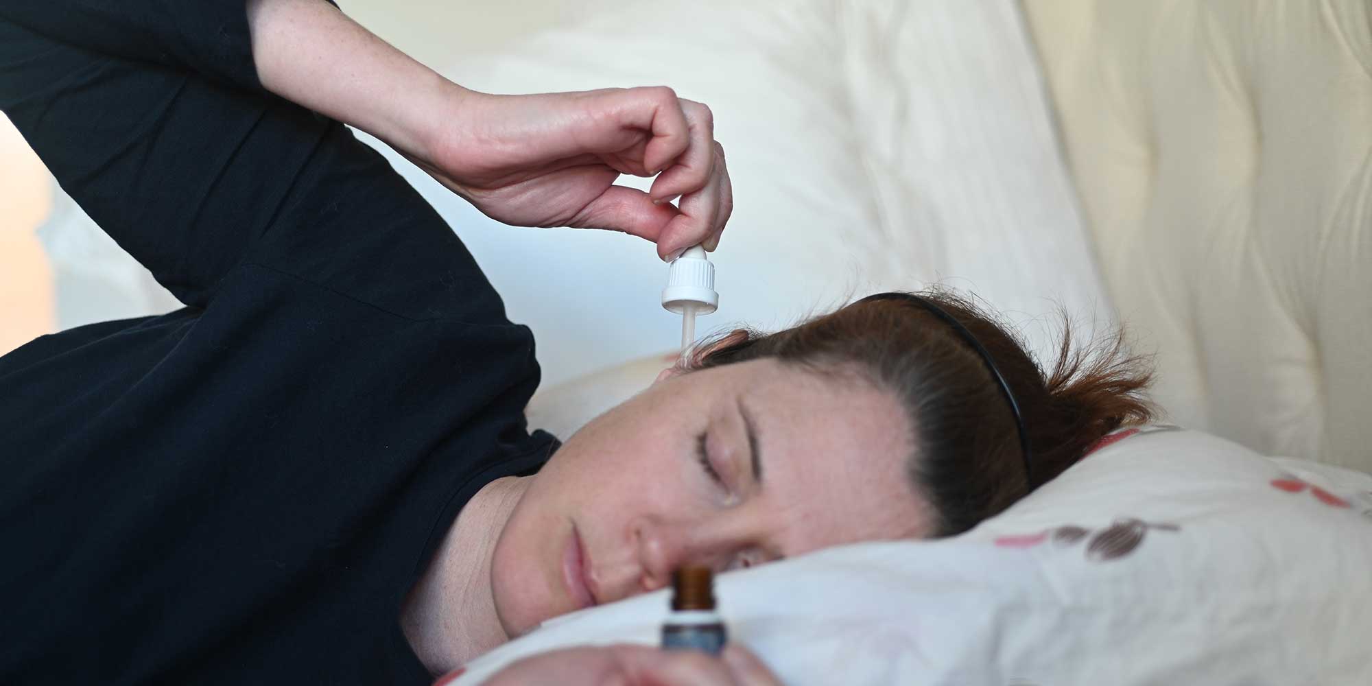 Woman lying down and putting olive oil drops in her ear