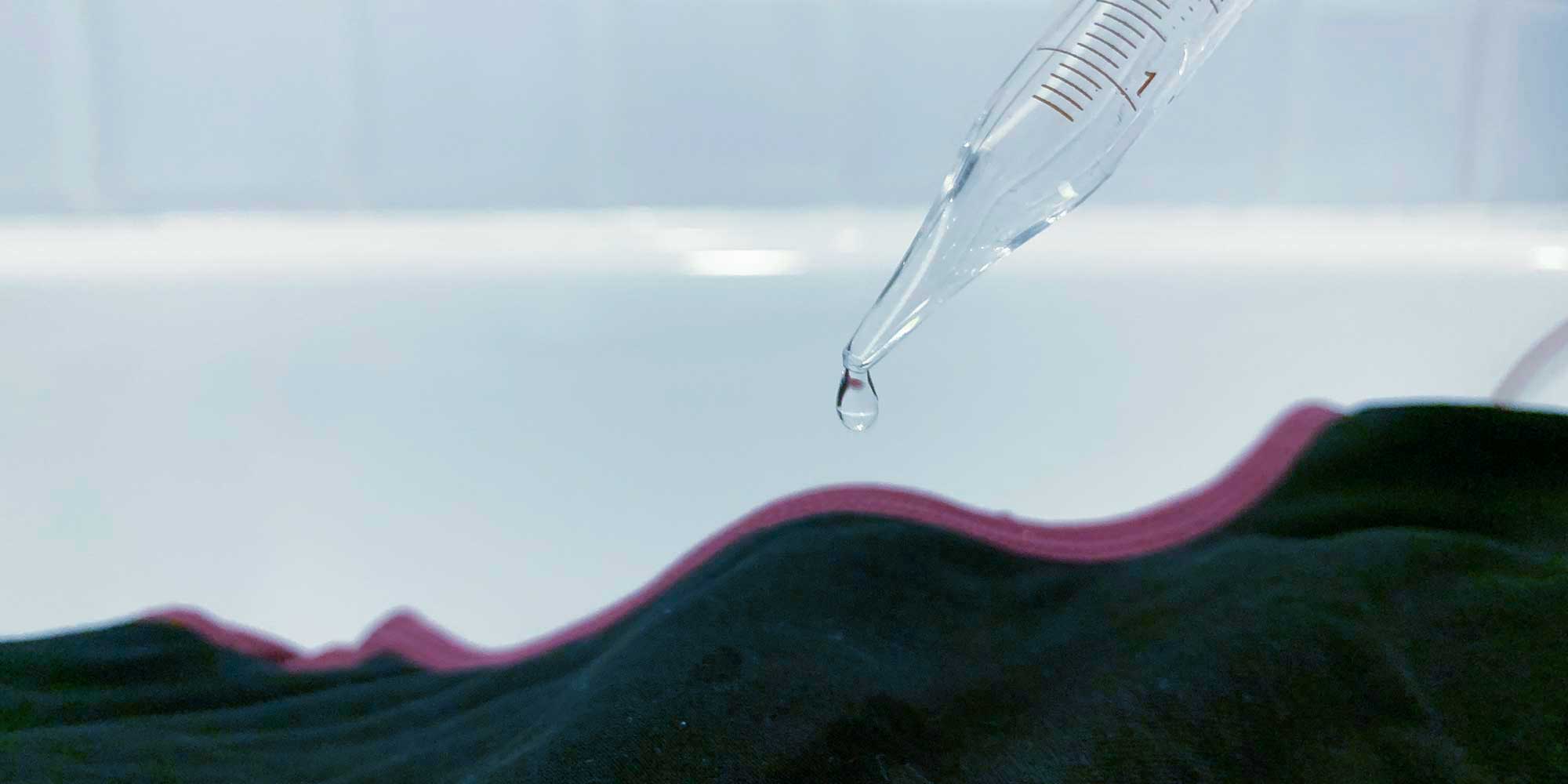 A drop of liquid falls from a clear measuring tube into a black gusset of a period pant