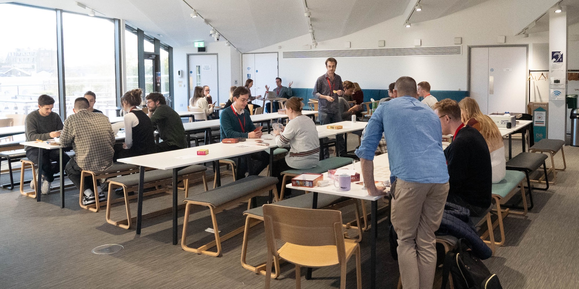 Group of people seated at tables in a room, engaged in playing board games