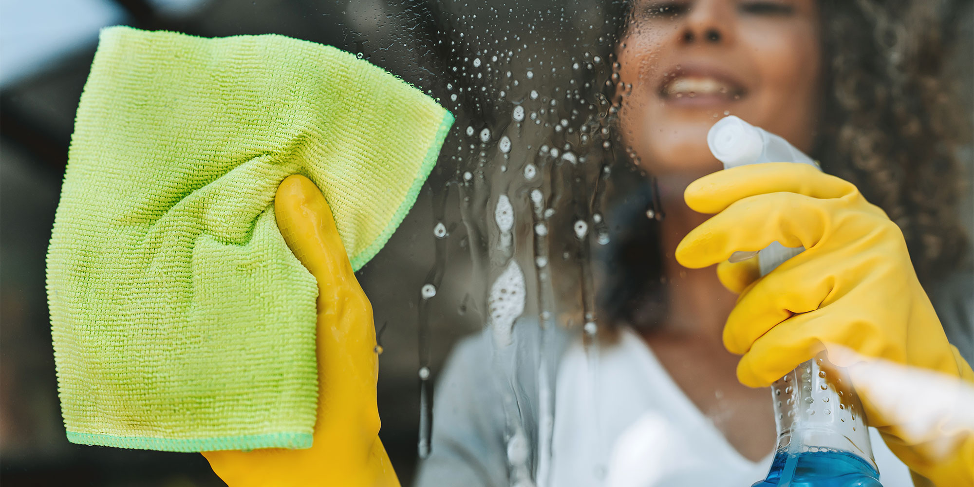 A woman cleaning a glass pane with spray and a microfibre cloth