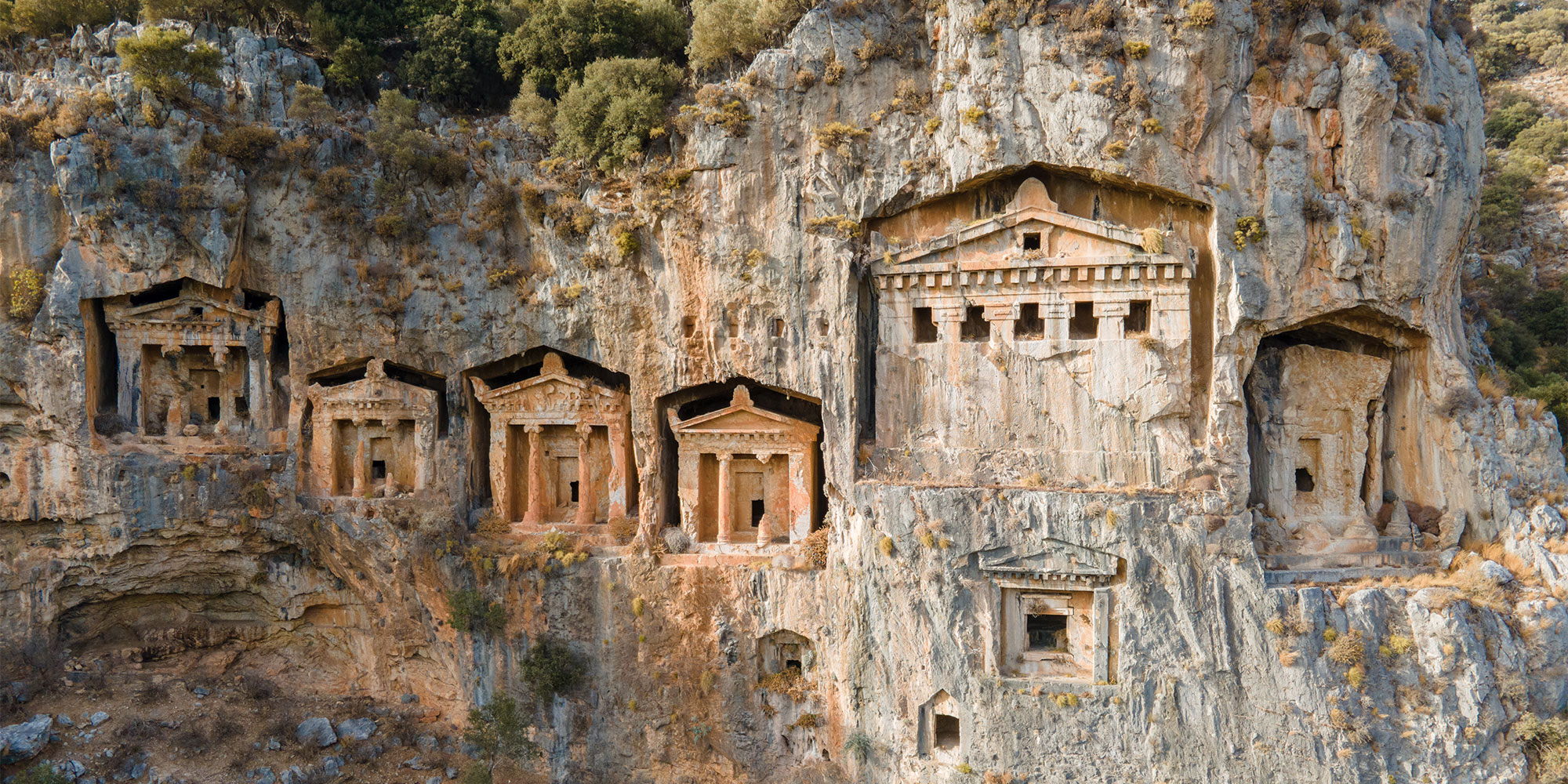 Ancient rock-cut tombs carved into a cliff face, showcasing historical architecture and craftsmanship.