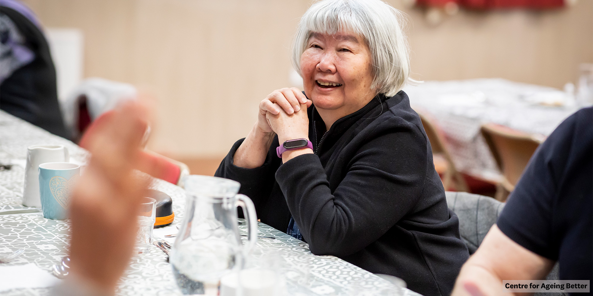 Woman sitting at a table and smiling, wearing a smart watch