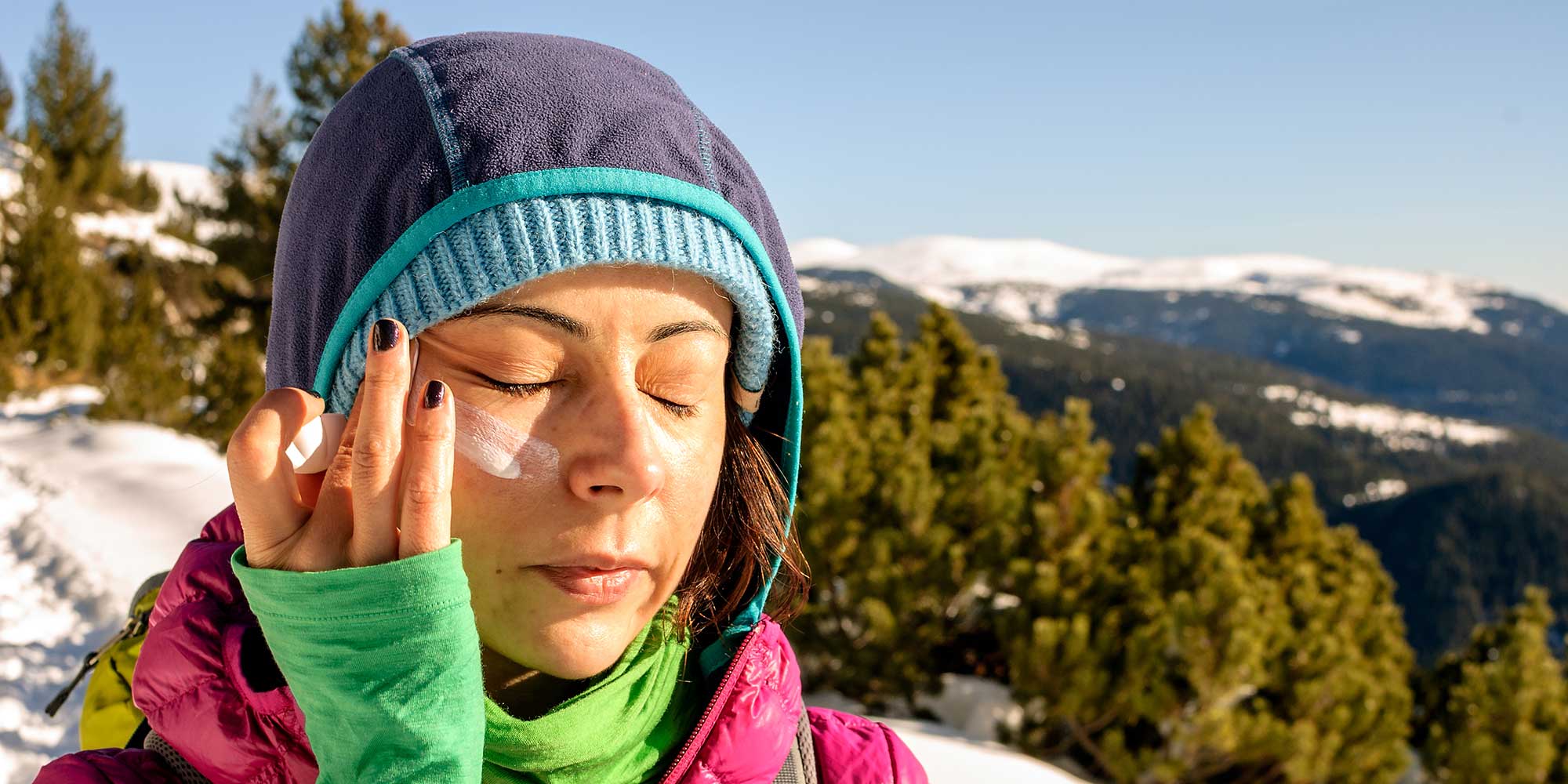 Woman applying sunscreen on her face in a mountain or ski setting