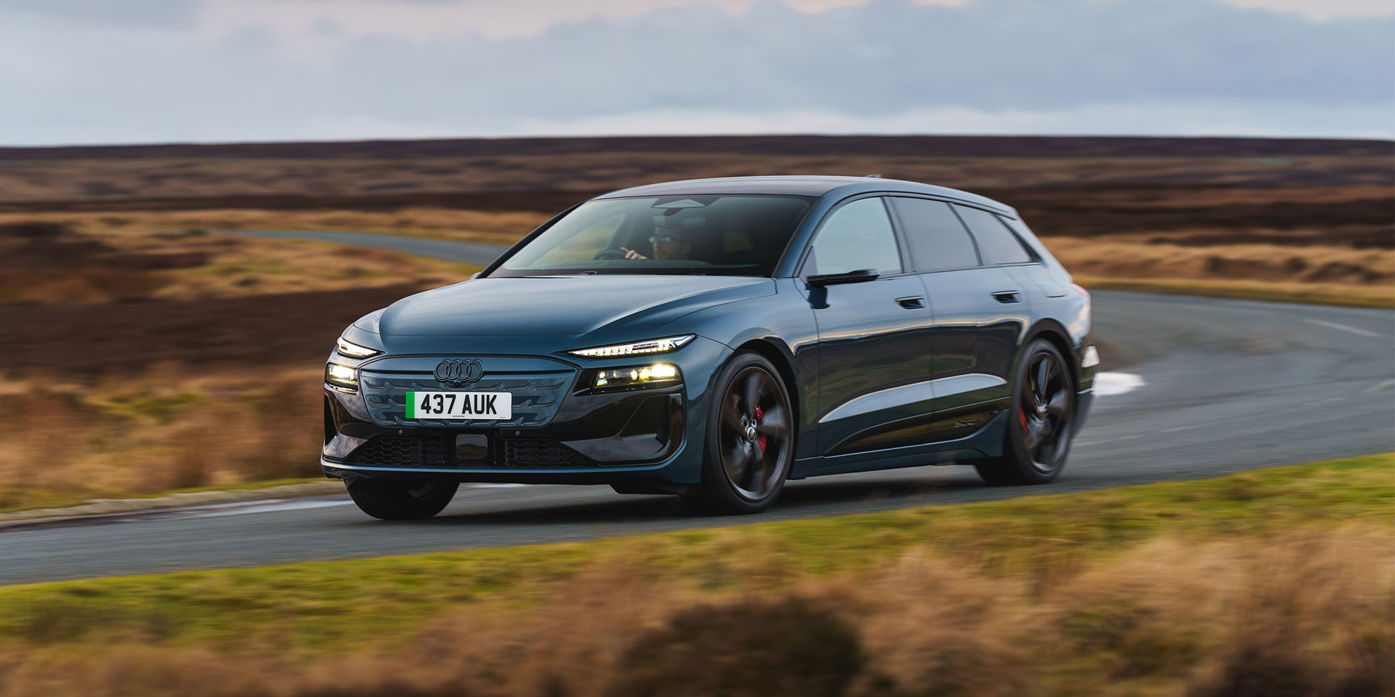 A blue Audi A6 Avant e-tron drives along a country road