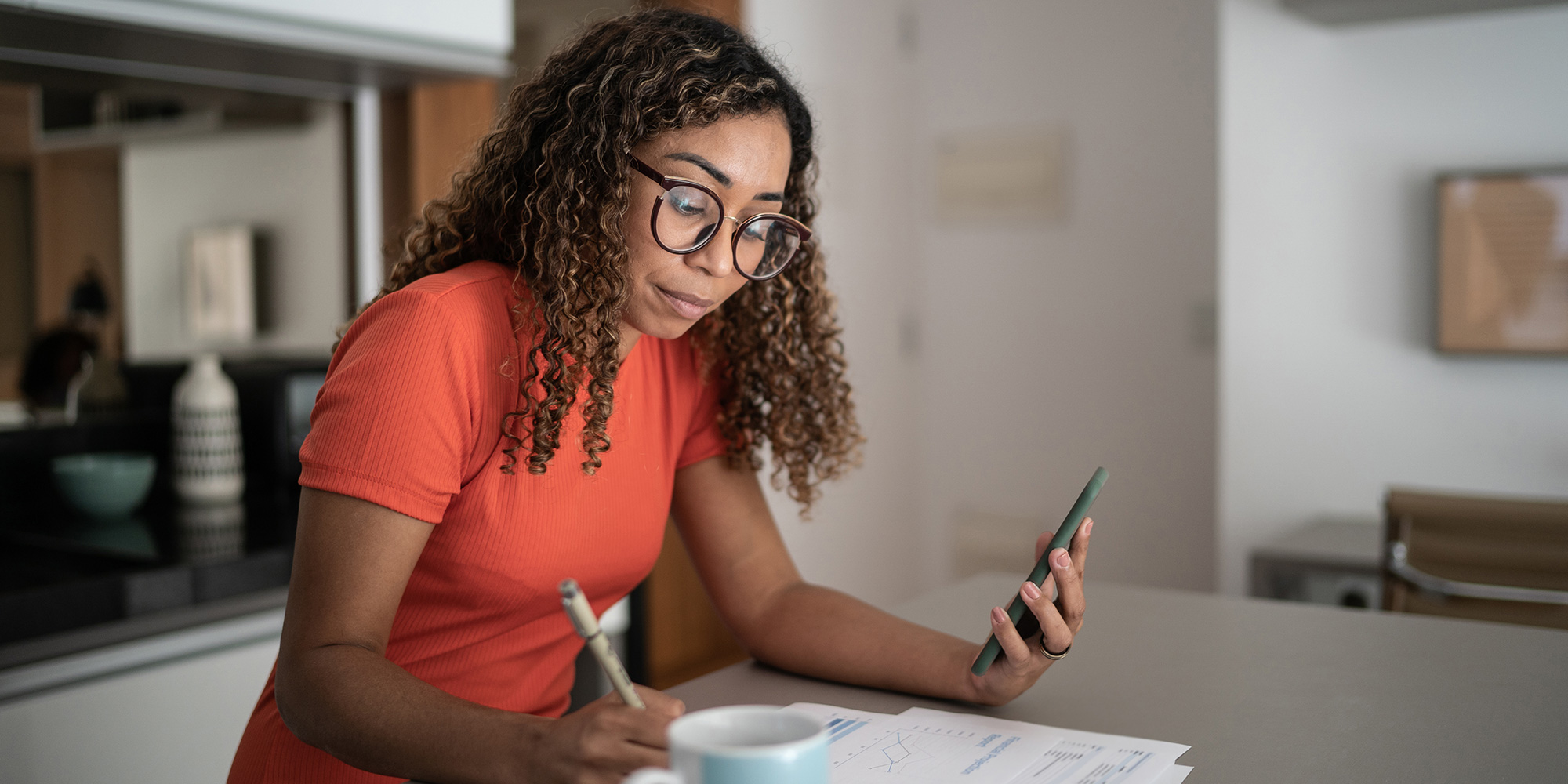 A woman writing on a piece of paper and looking at her phone